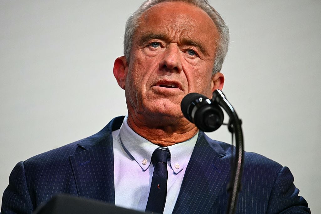 An older man in a suit speaks into a microphone.