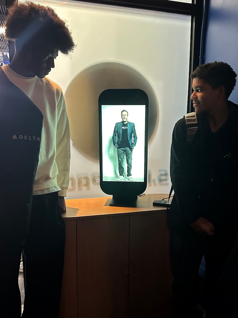 Two students look at a screen with a man standing up.