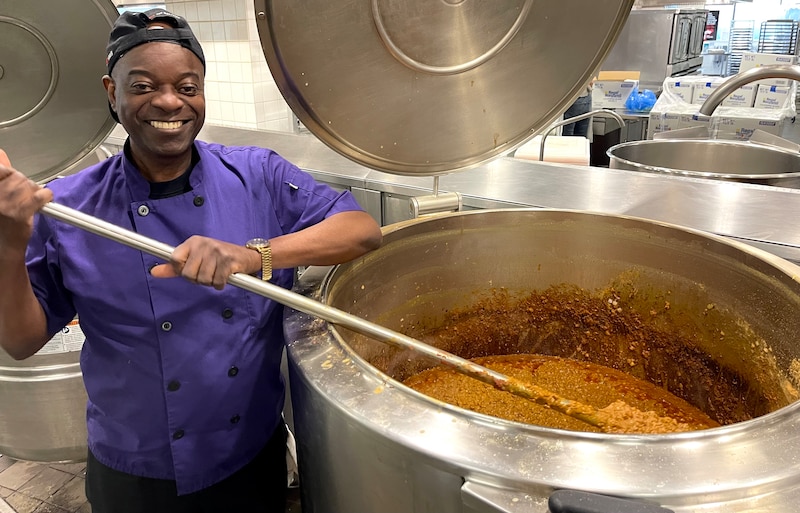 A chef stirs a giant pot of stew in a kitchen.