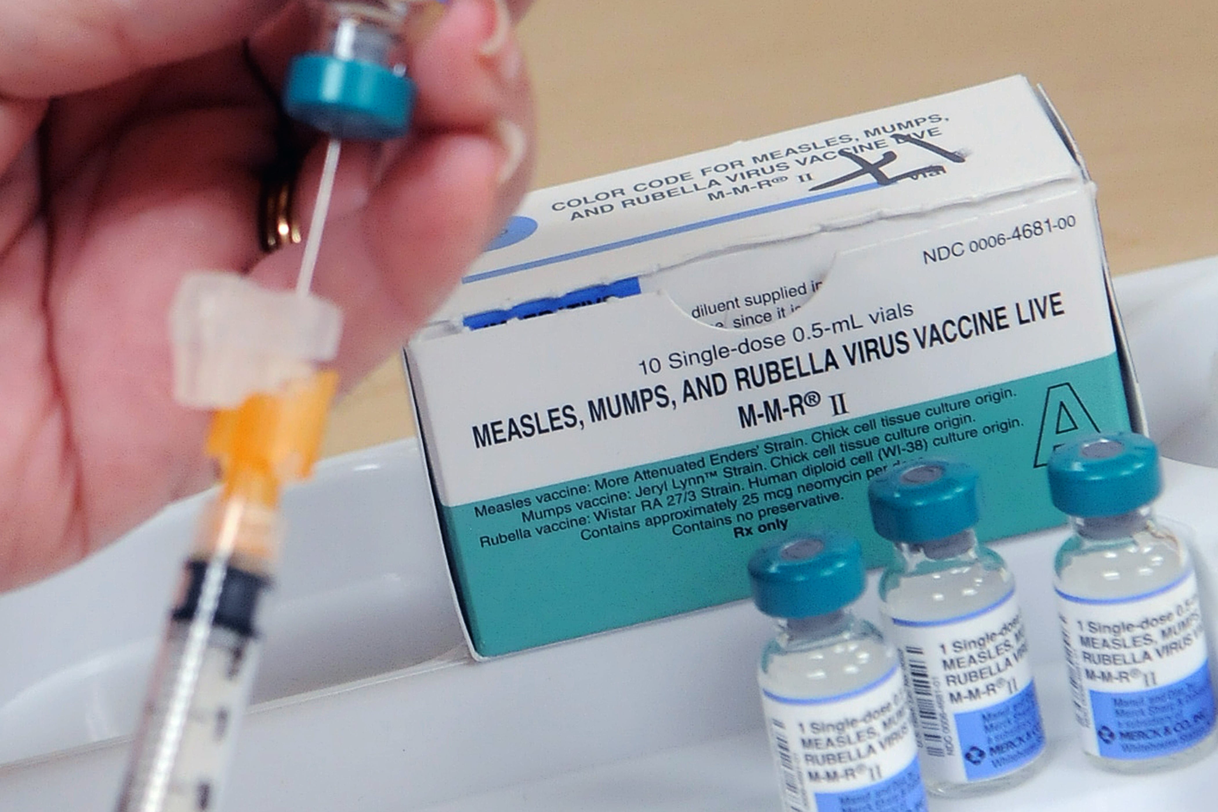 A close up of a box of medicine and a pair of hands holding a syringe.