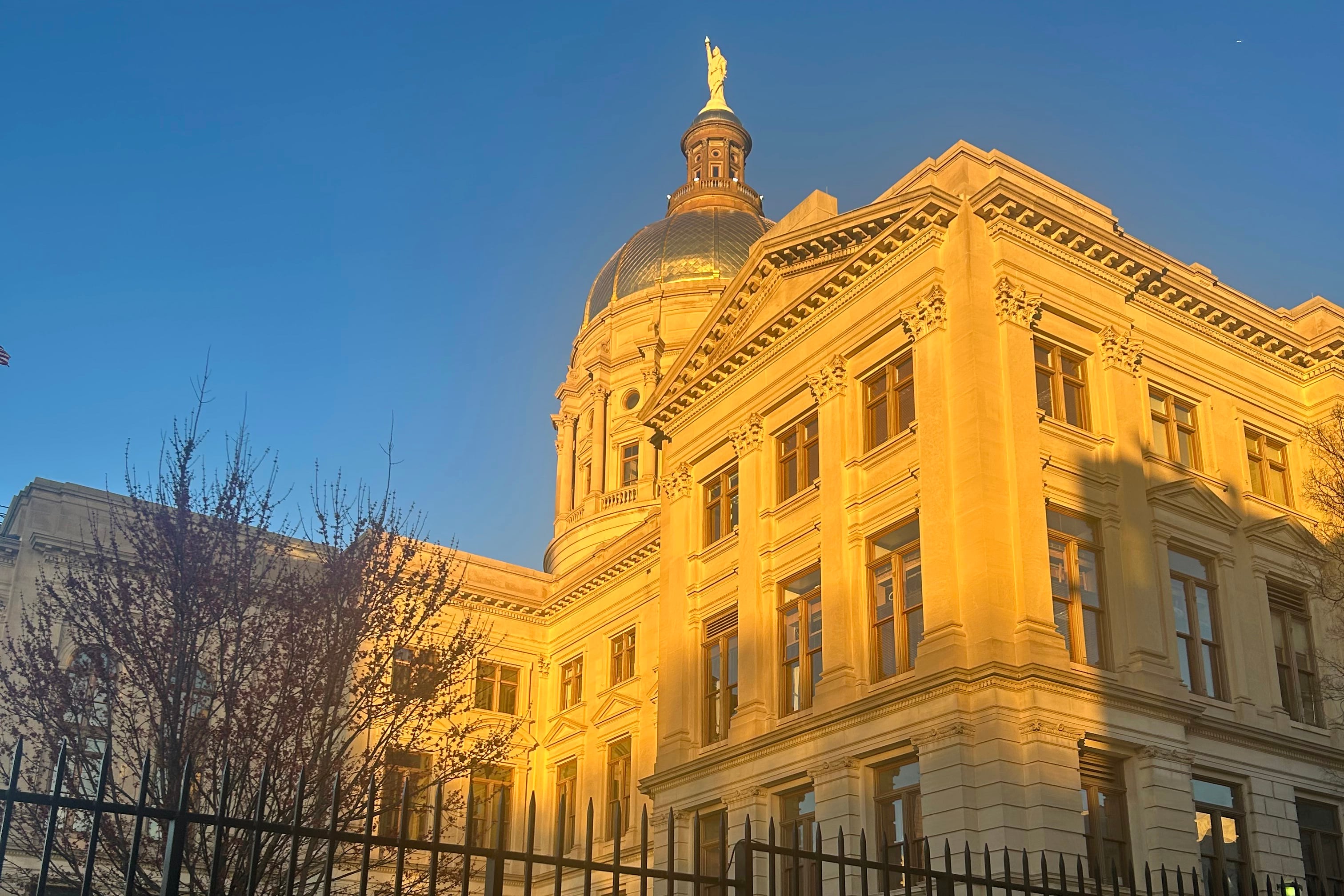 Sun illuminates a side of a large dome state capitol building.