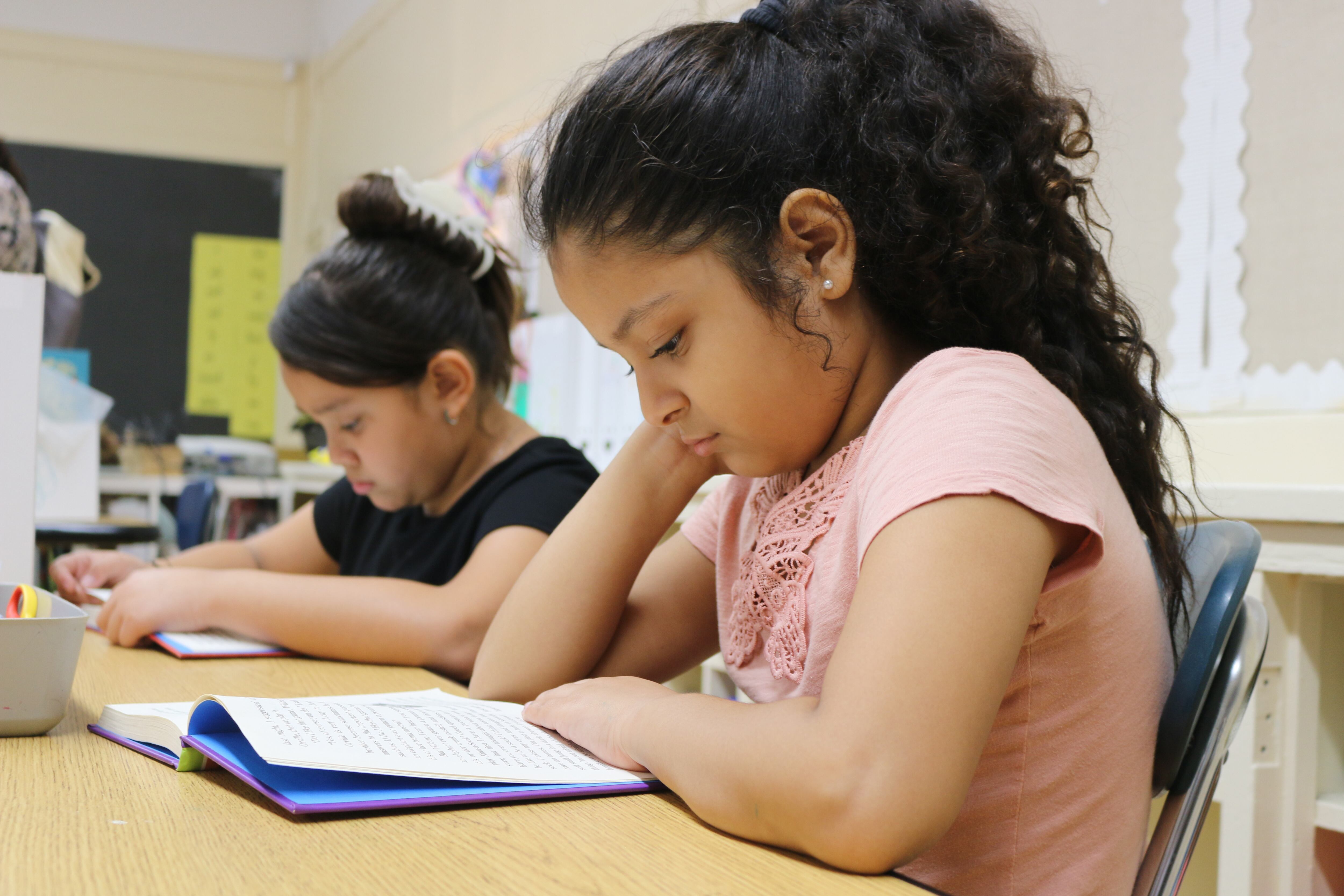 Two students read at a table in a classroom.