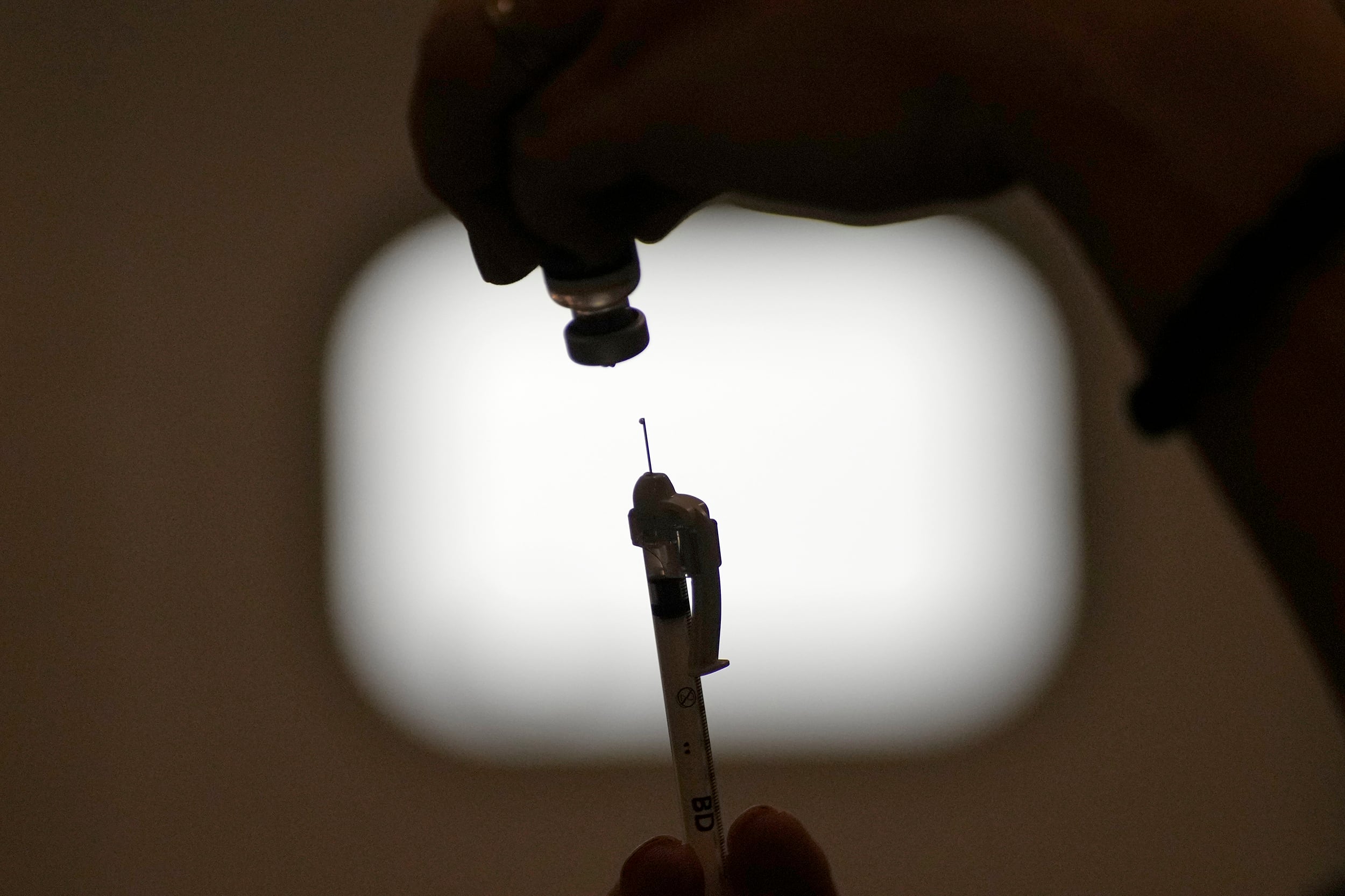 A syringe is pulled out of a vaccine vial.