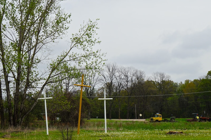 Crosses stand in a field near a small church.