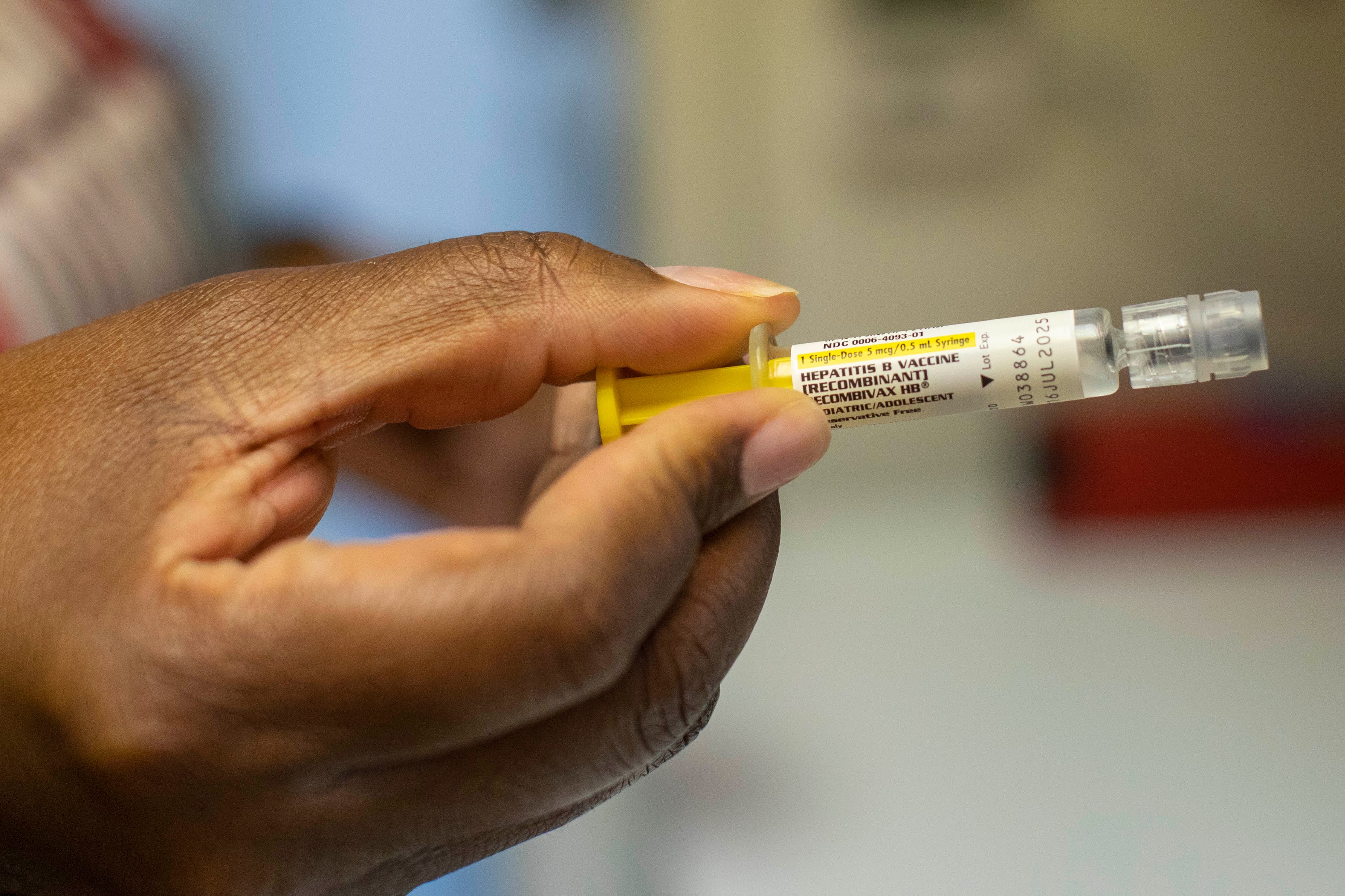 A hand holds a vial of hepatitis B vaccine.