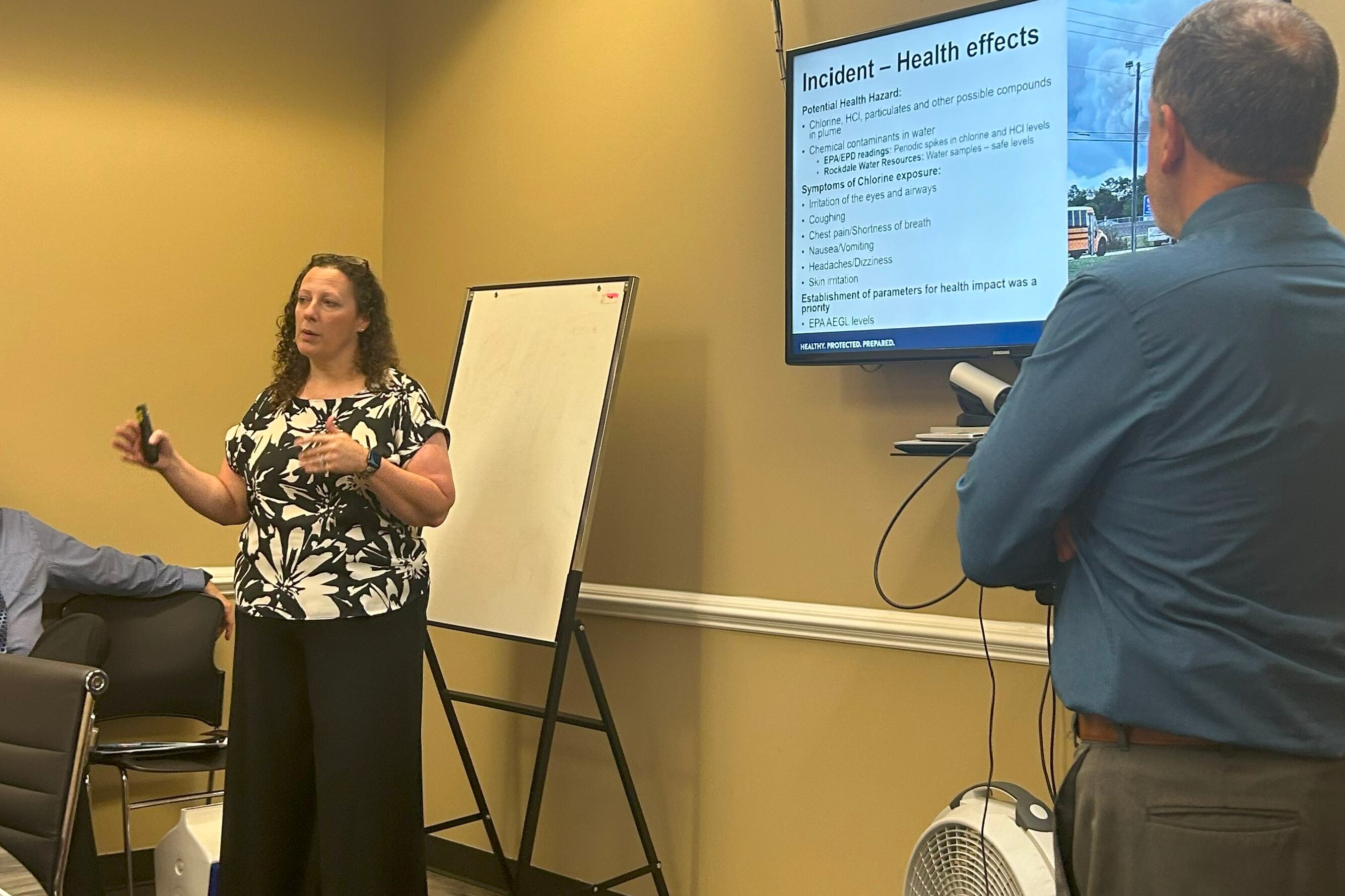 Two health officials stand in front of a projector to speak at a health department meeting.