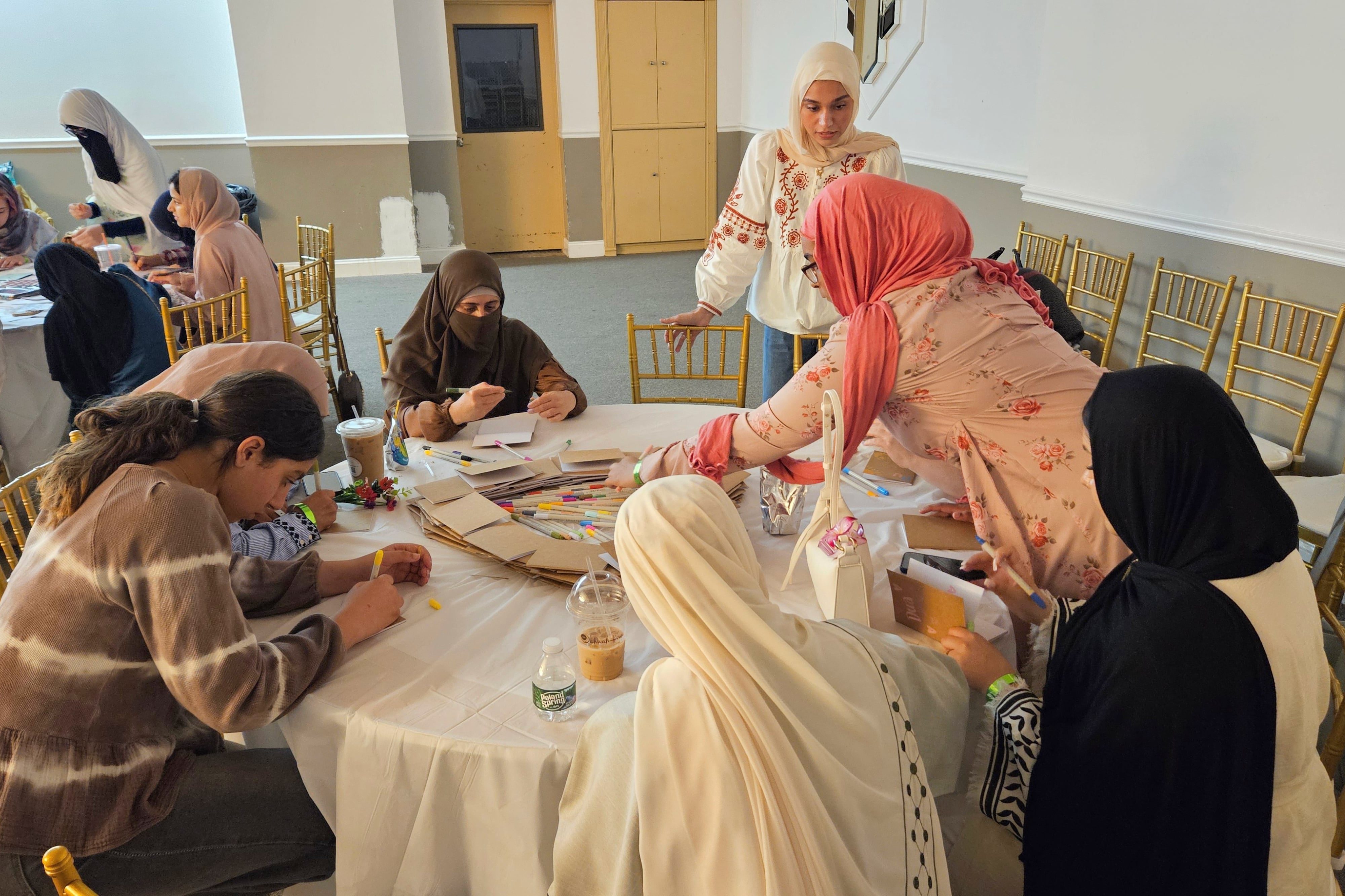 Women and girls do crafts around a round table.