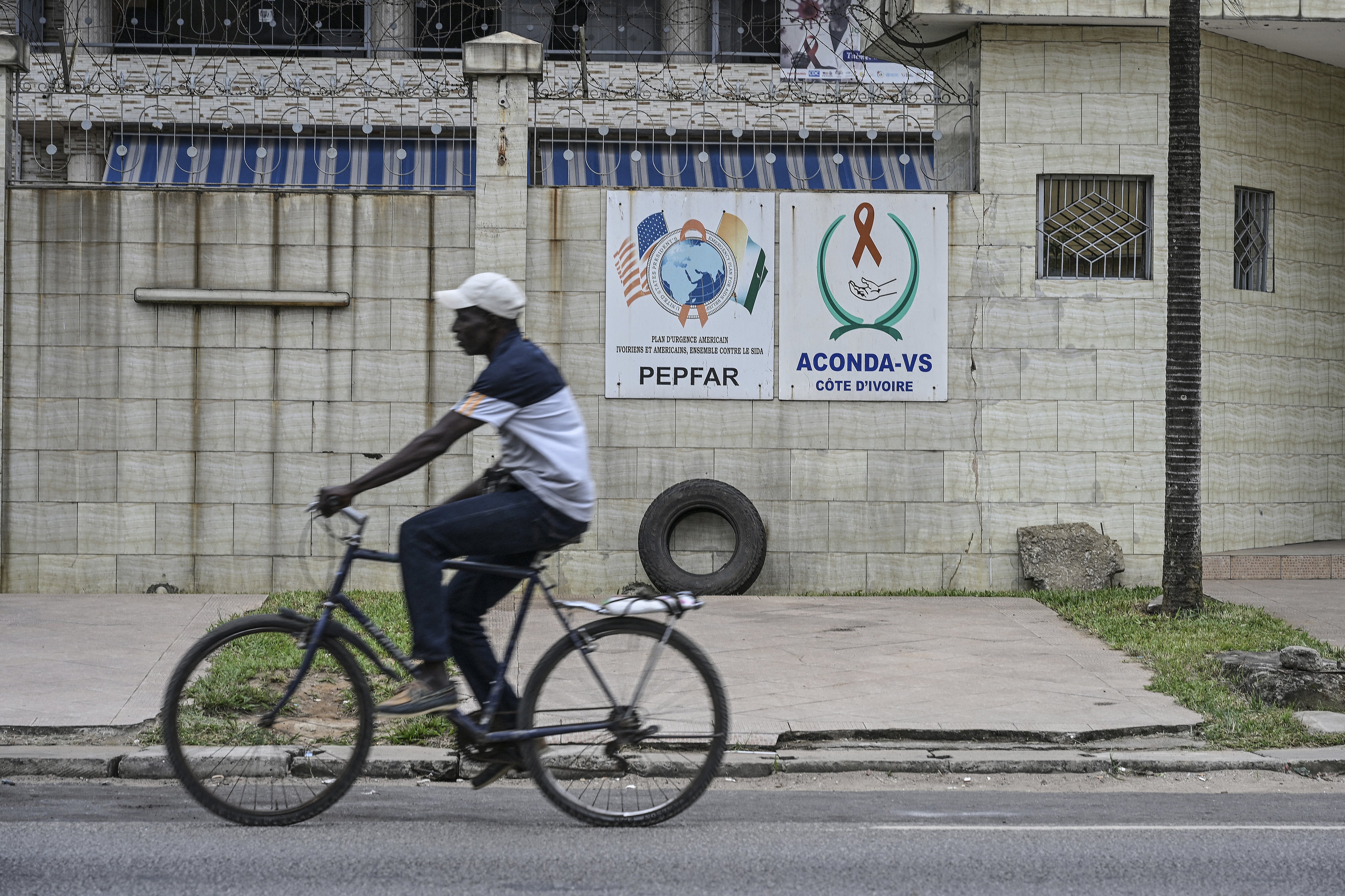 A bicyclist rides past a PEPFAR sign.