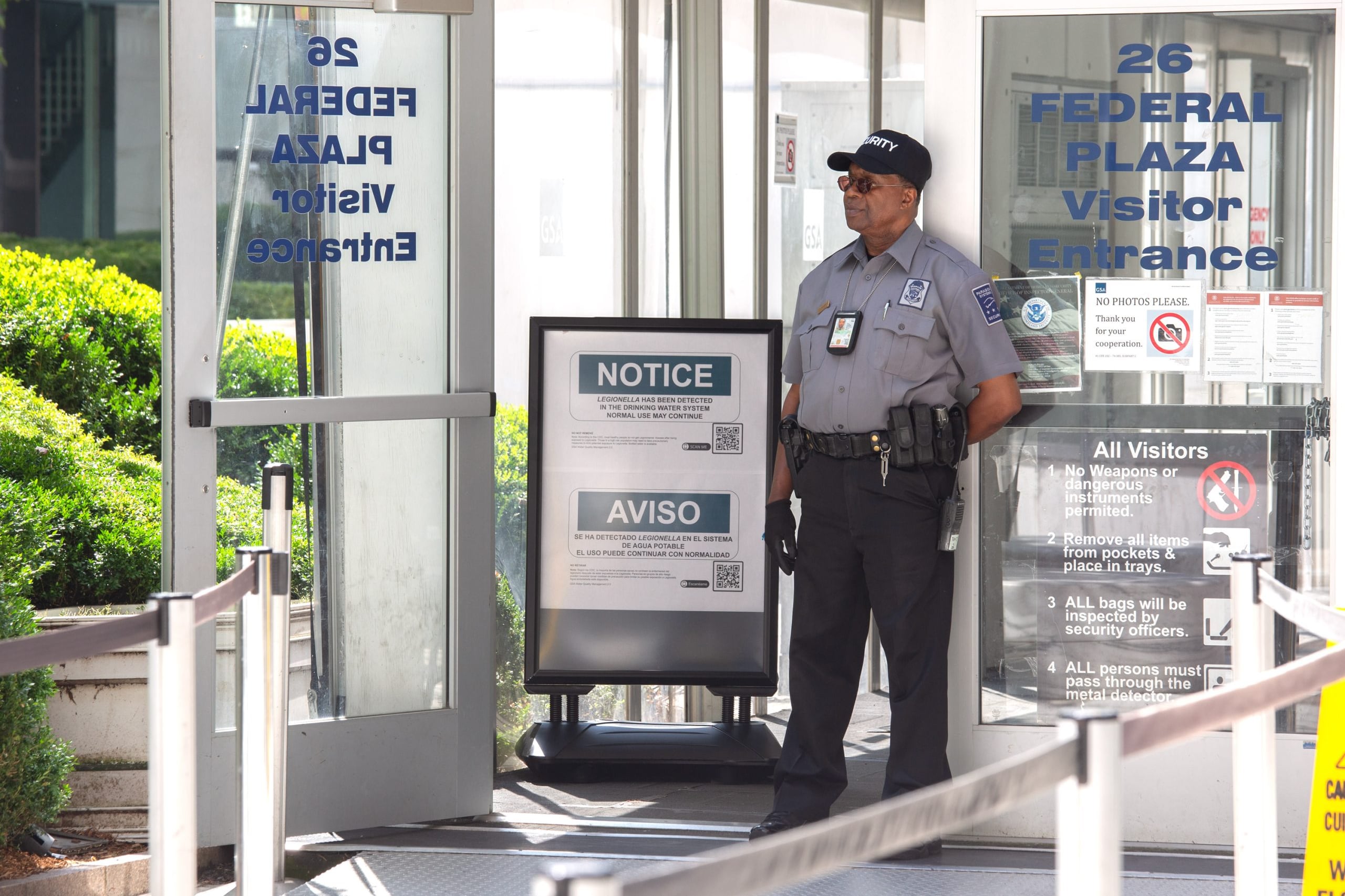 A security guard stands next to an entrance of a federal office building next to a sign warning of water contamination.