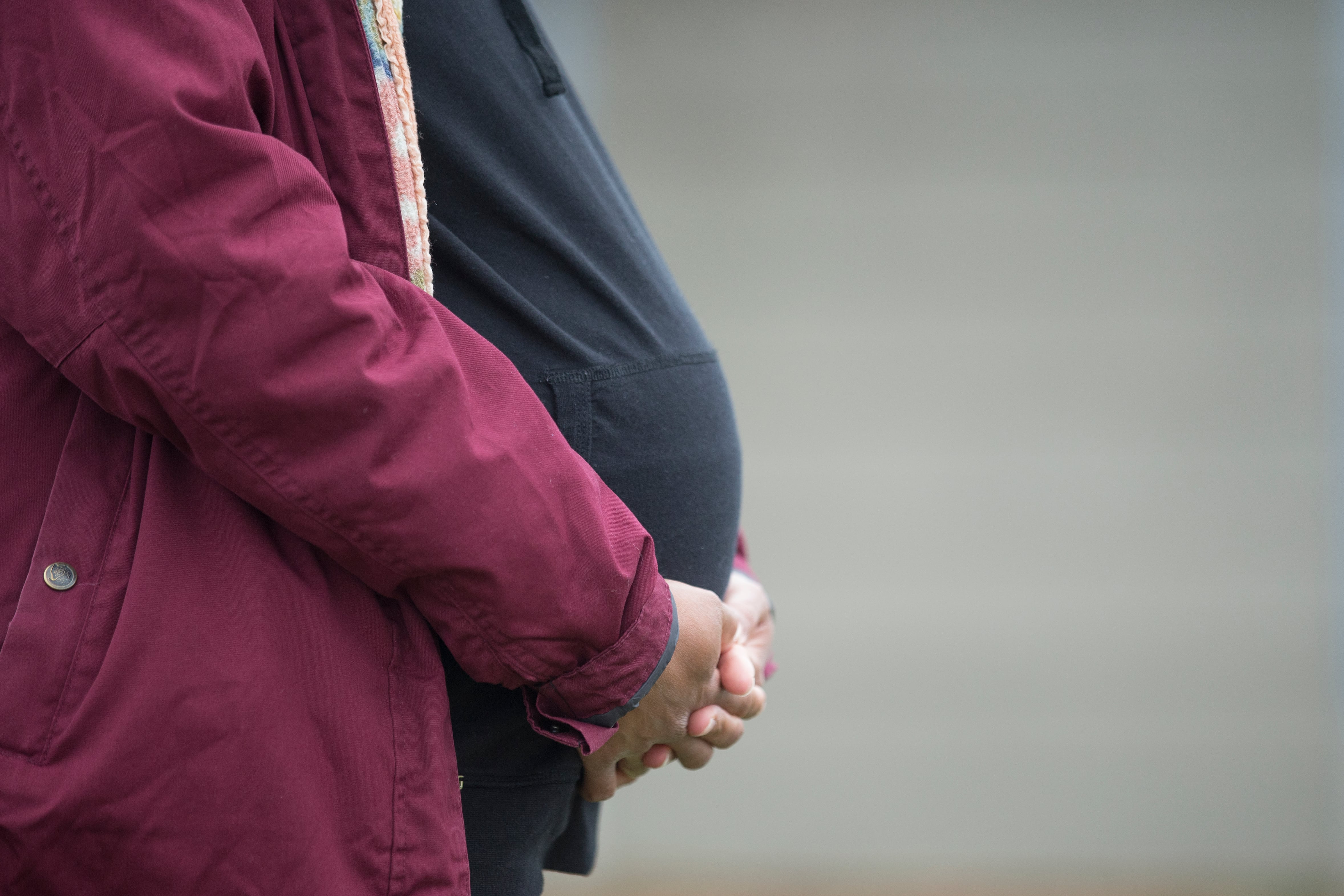 A pregnant woman clasps her hands around her belly.