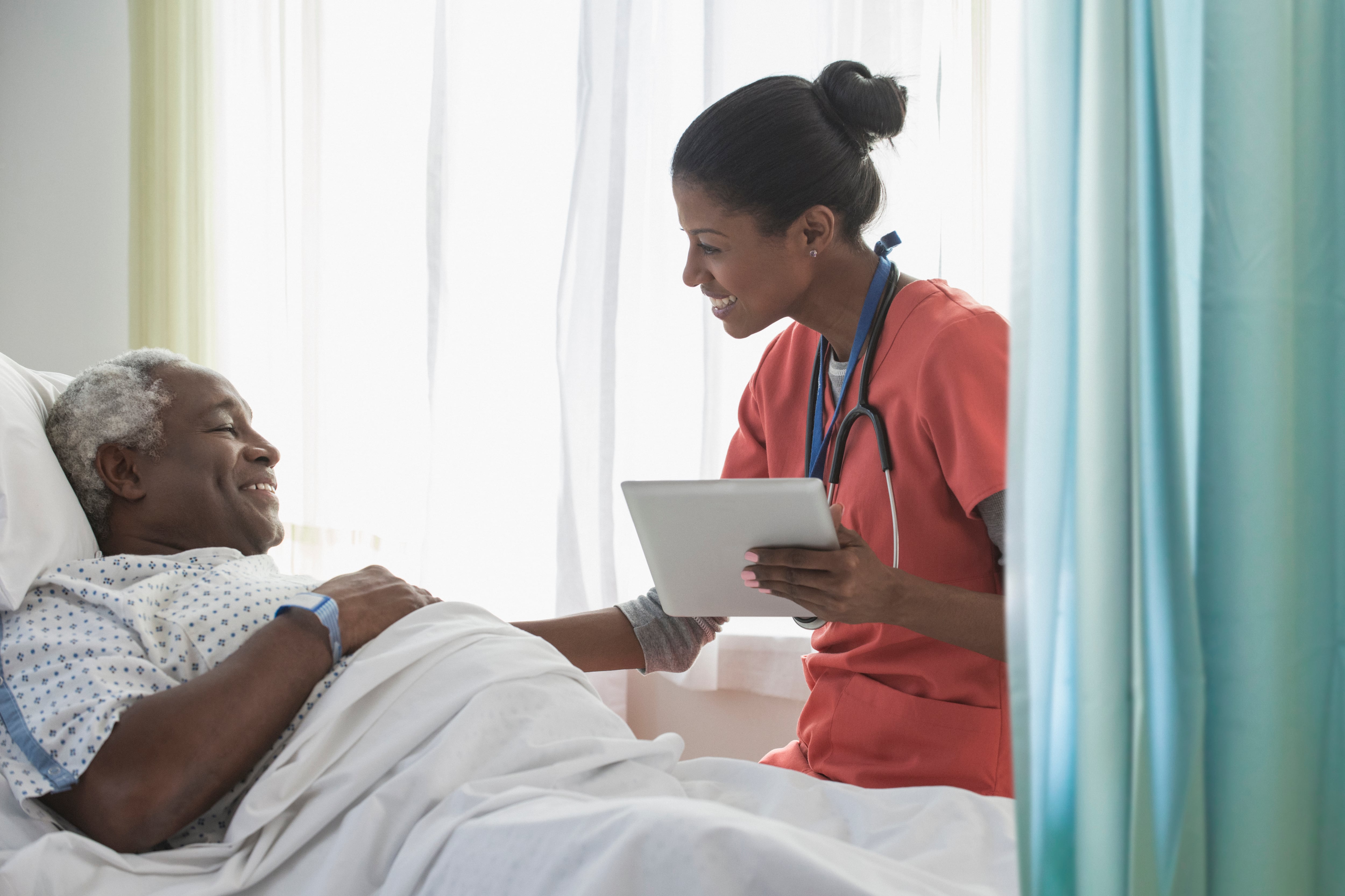 A patient lies in a hospital bed next to a nurse standing beside him.