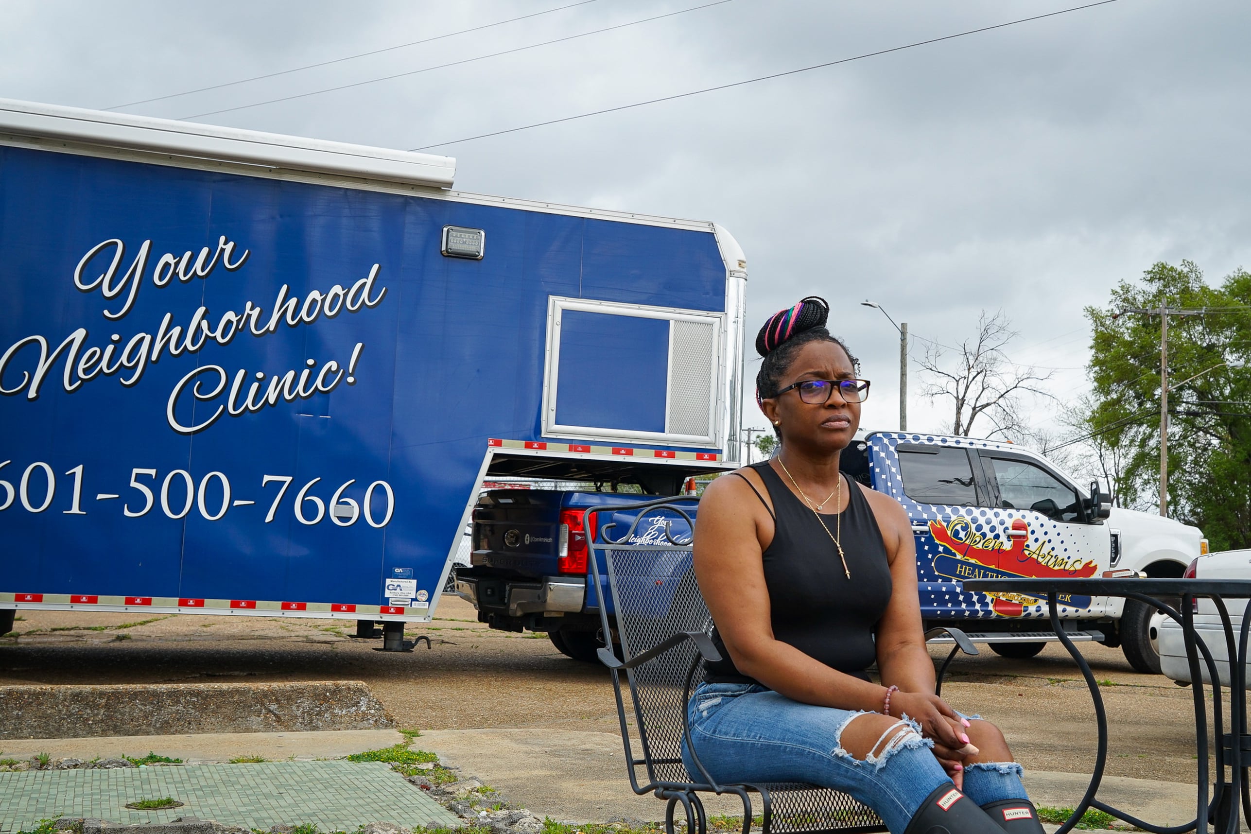 A woman sits in front of a trailer that serves as a mobile clinic.