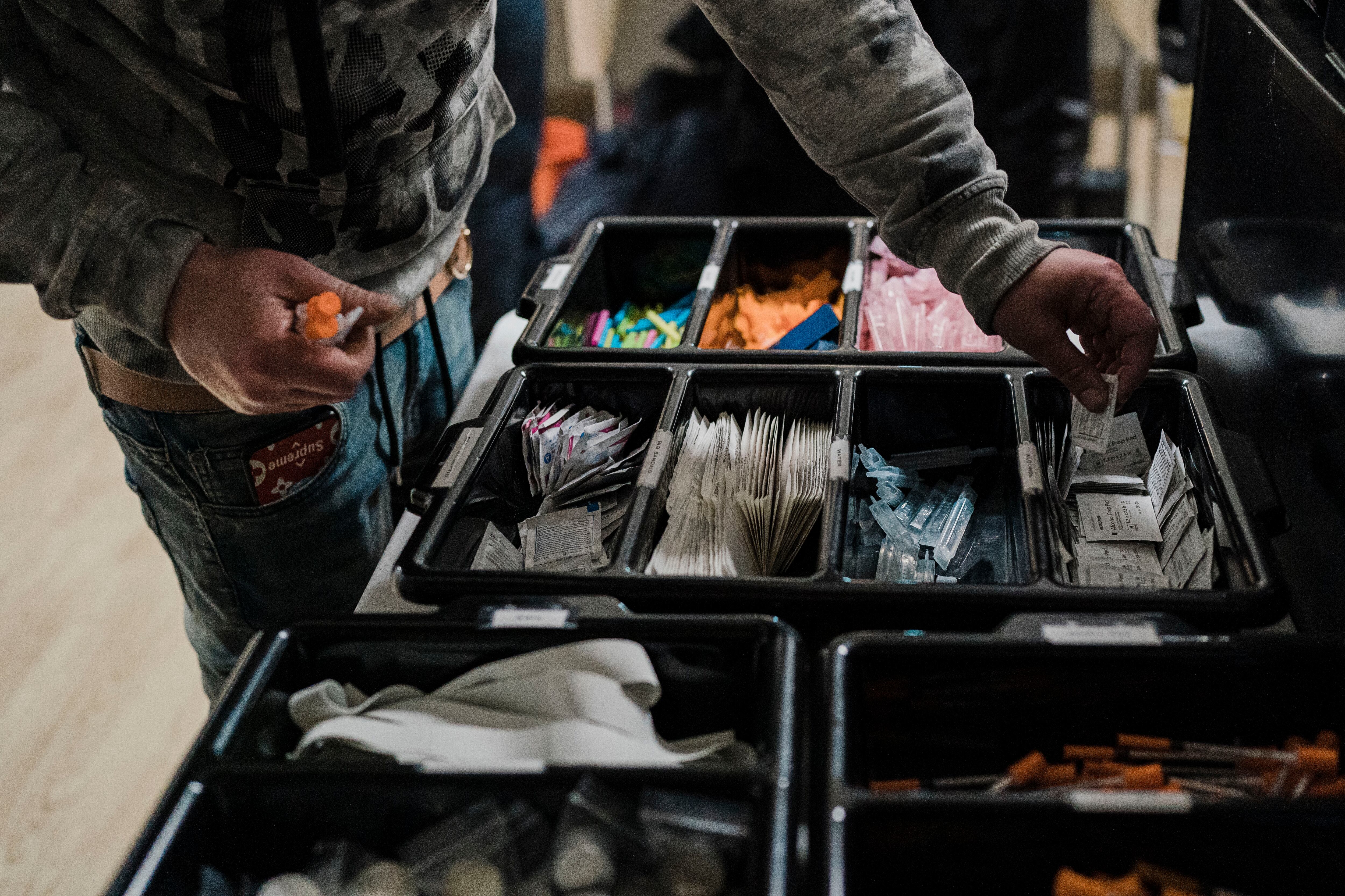 A man picks up syringes and other supplies from a tray.