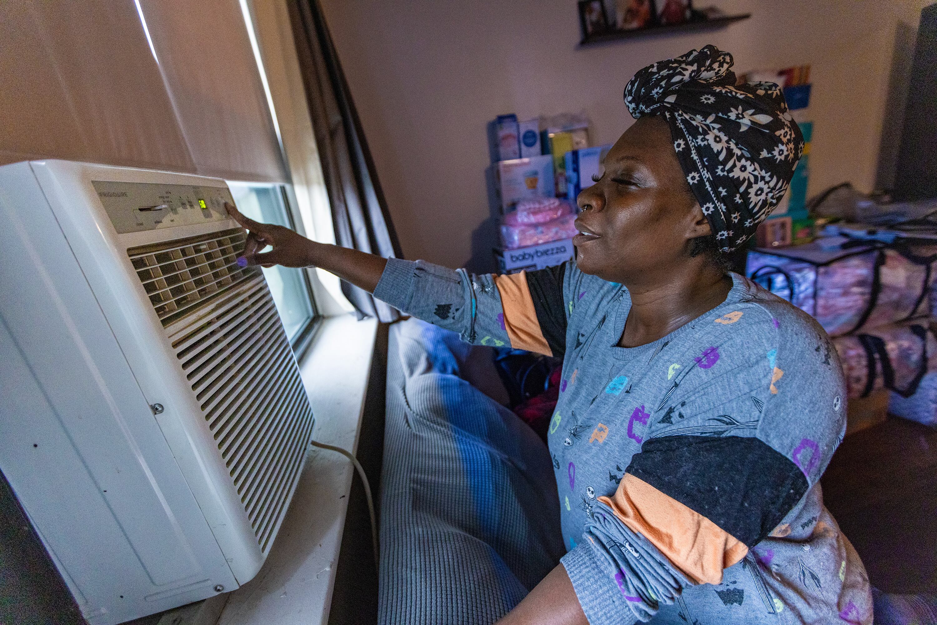 A woman stands in front of a window air-conditioning unit.