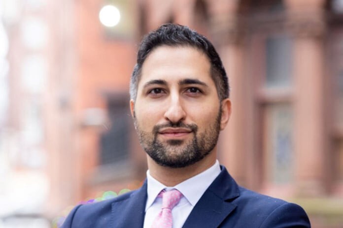 A man in a blue suit and red tie stands outside of a building posing for a portrait.