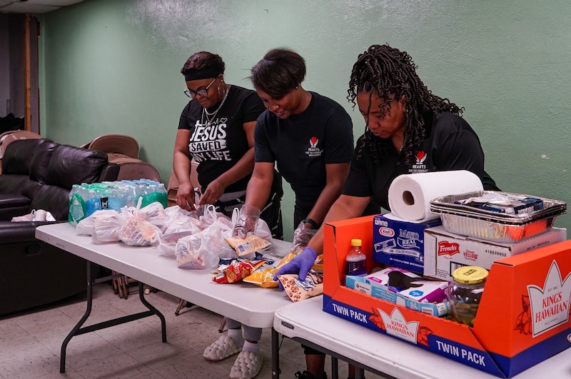 Three women put out food on a table.