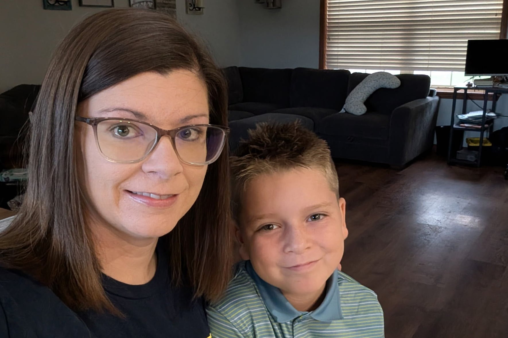 A white woman wearing glasses poses for a selfie with her son in their living room.