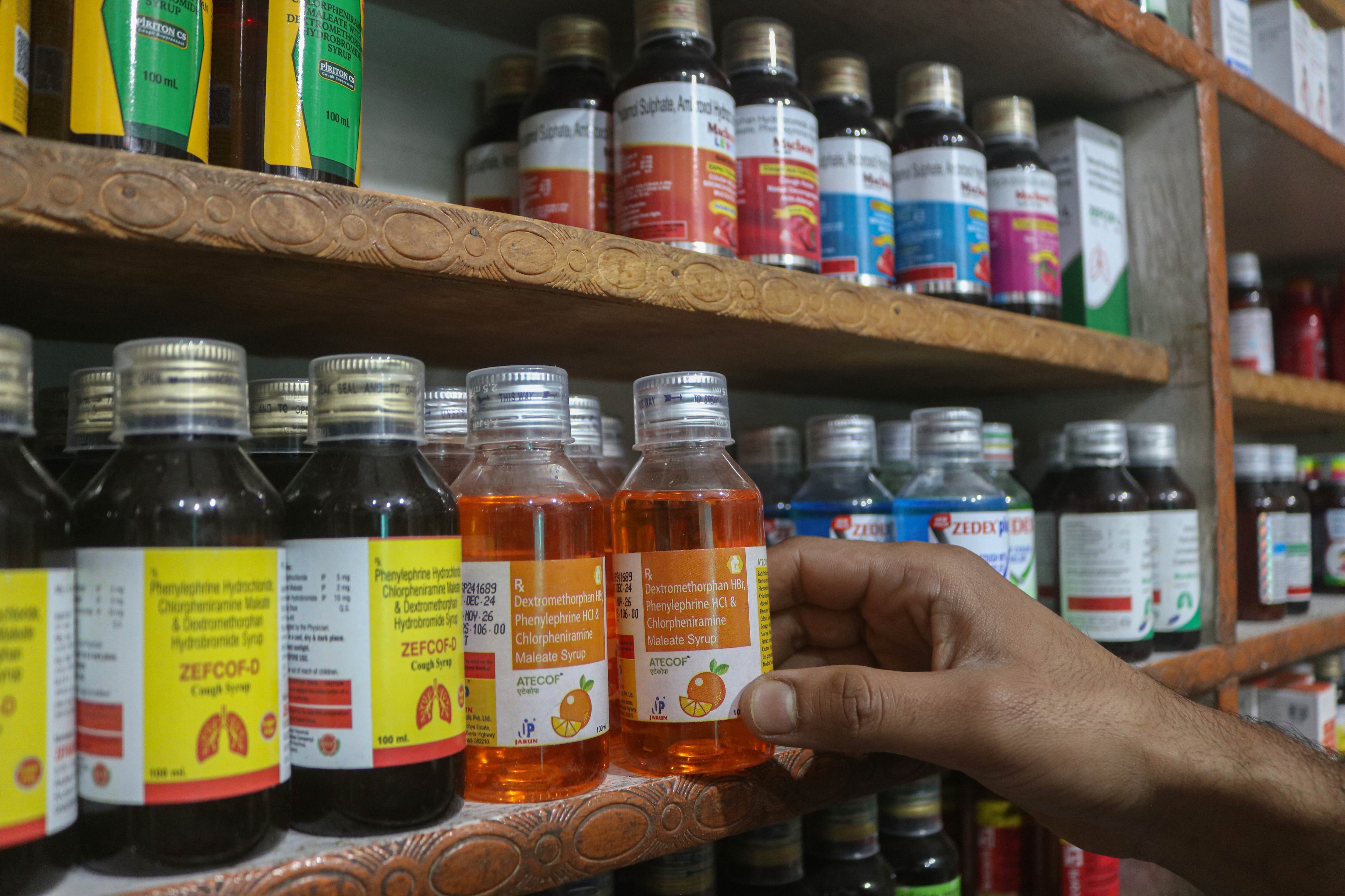 A hand touches a bottle of cough syrup on a store shelf.