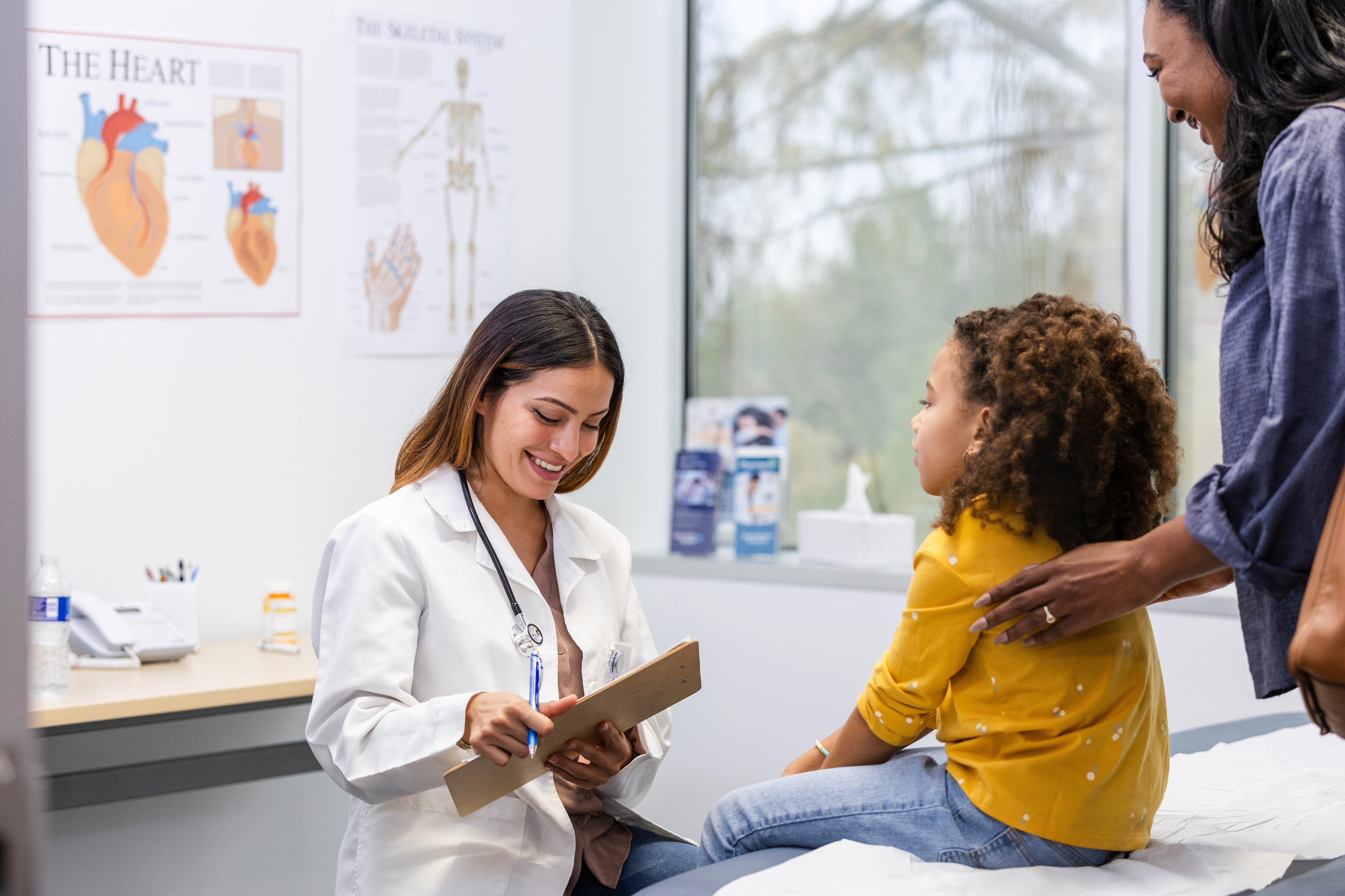 A doctor treats a child, accompanied by her mother, in a doctor's office exam room.