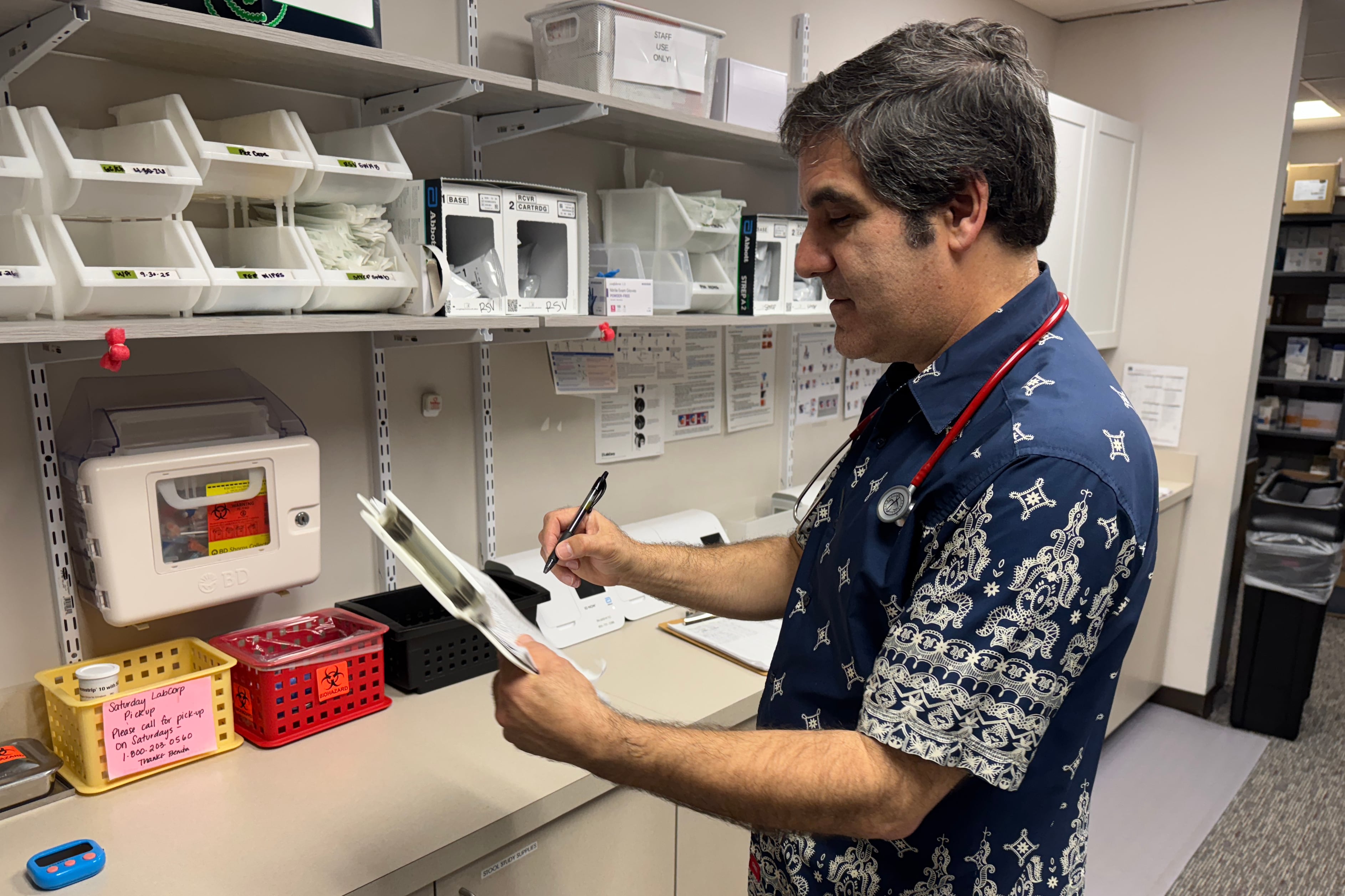A man in a colorful shirt and a stethoscope around his neck poses for a portrait in a medical lab.