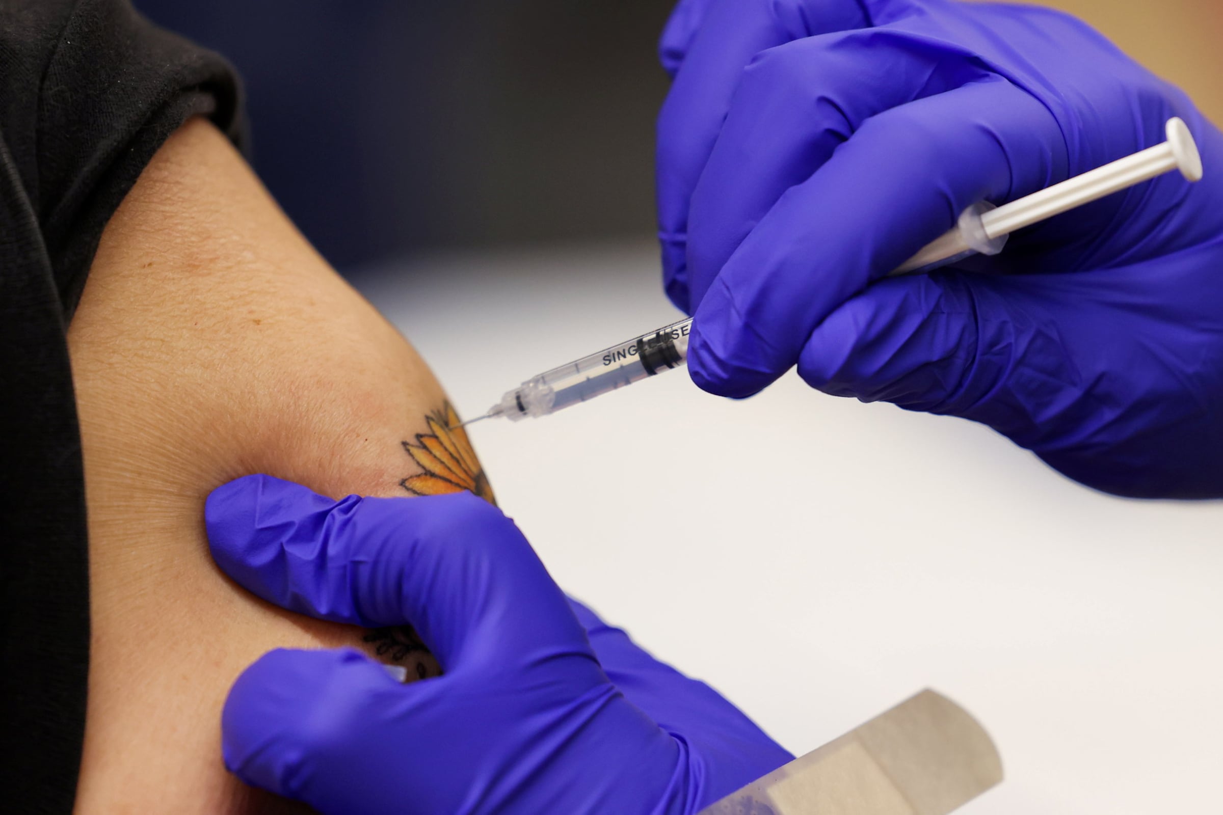 A Covid shot is administered into a person's arm with a flower tattoo.