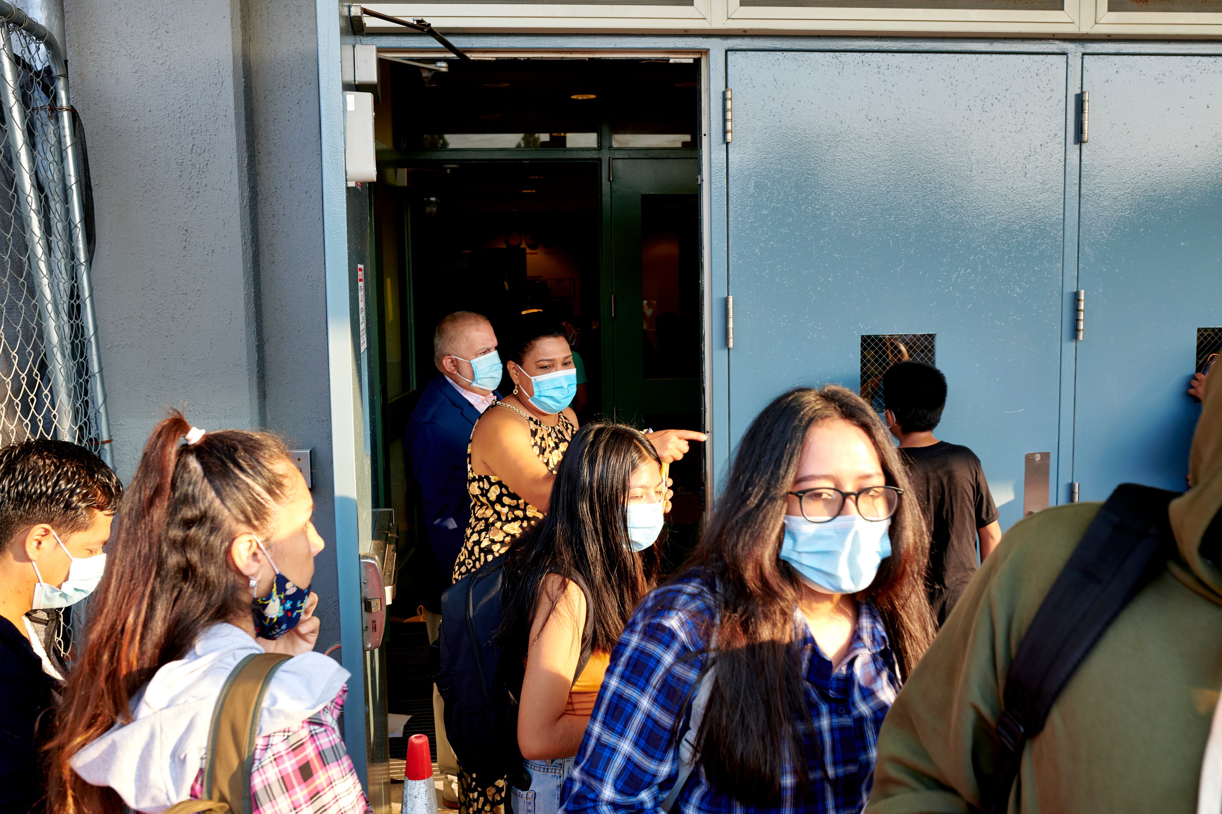 A group of students and staff stand outside of a school building wearing masks.