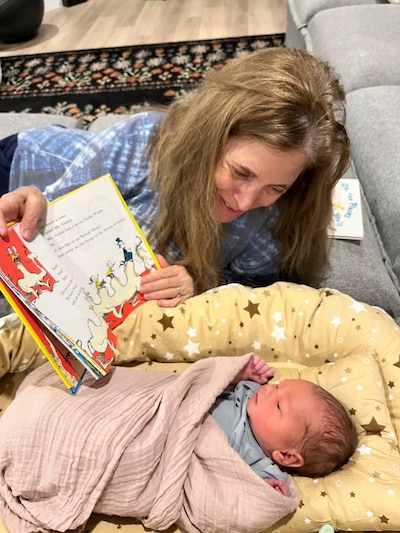 A white grandmother reading a picture book to an infant lying on a sofa.