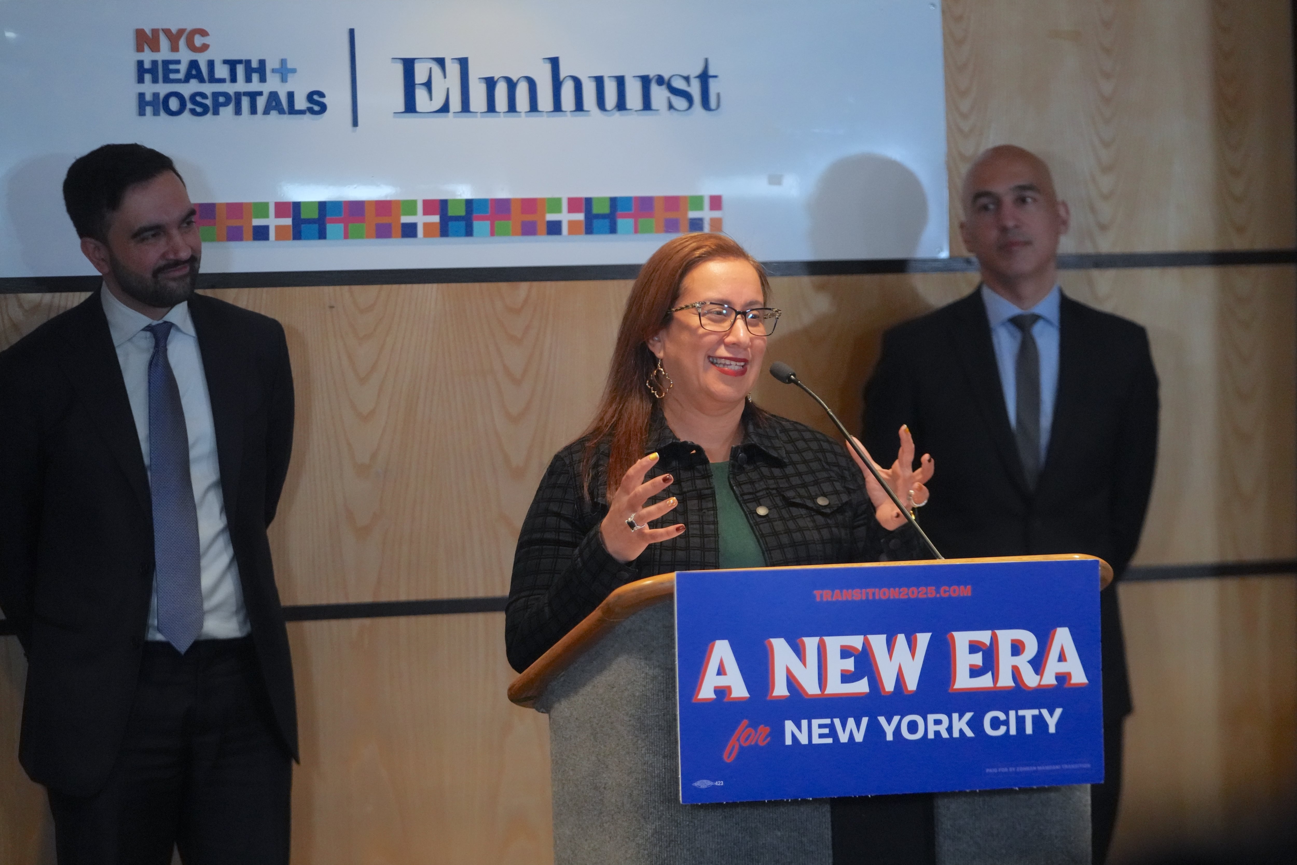 Dr. Helen Arteaga Landaverde speaks from a podium, with Mayor Zohran Mamdani standing behind her.