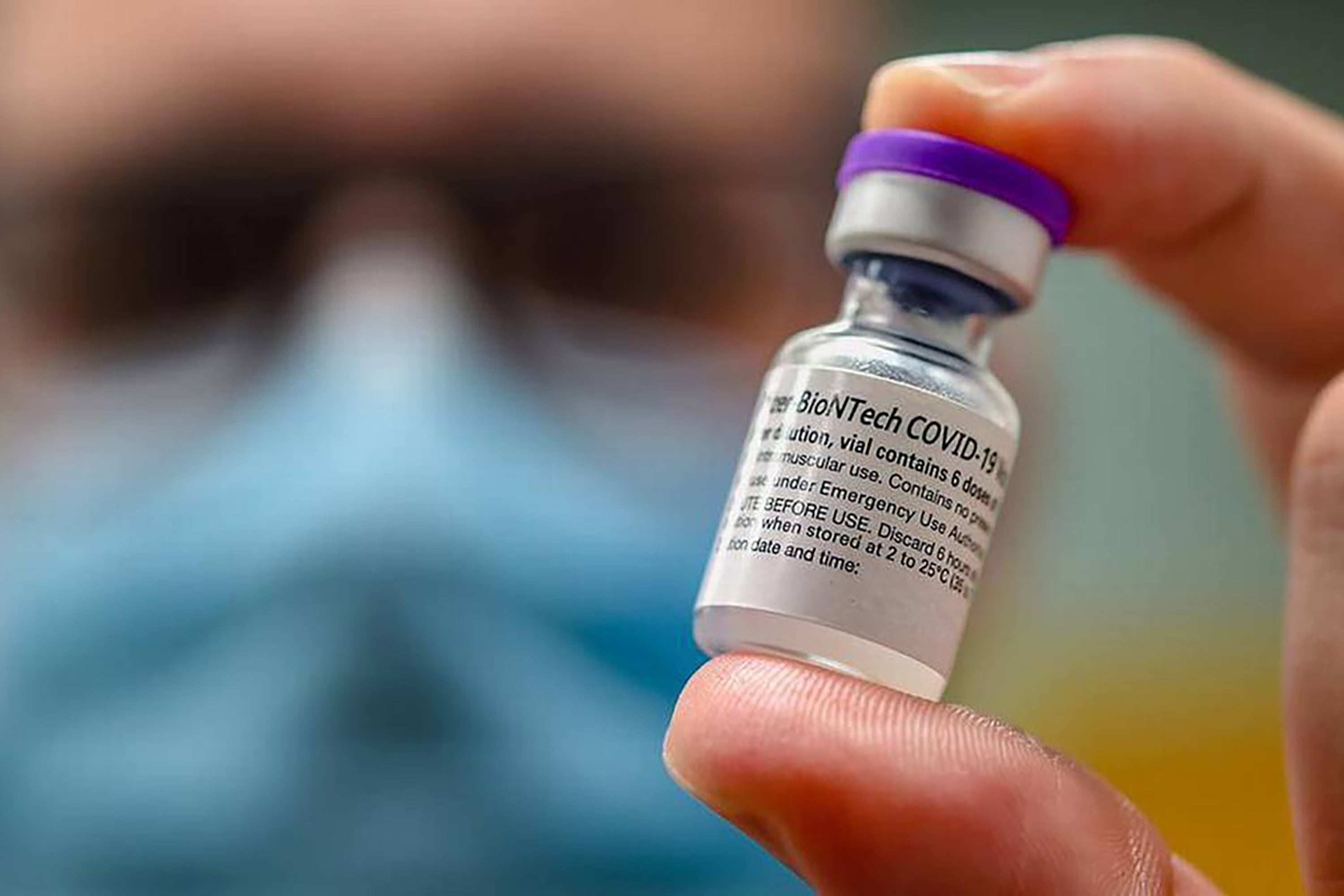 A person wearing a face mask holds up a a vial of Covid vaccine.