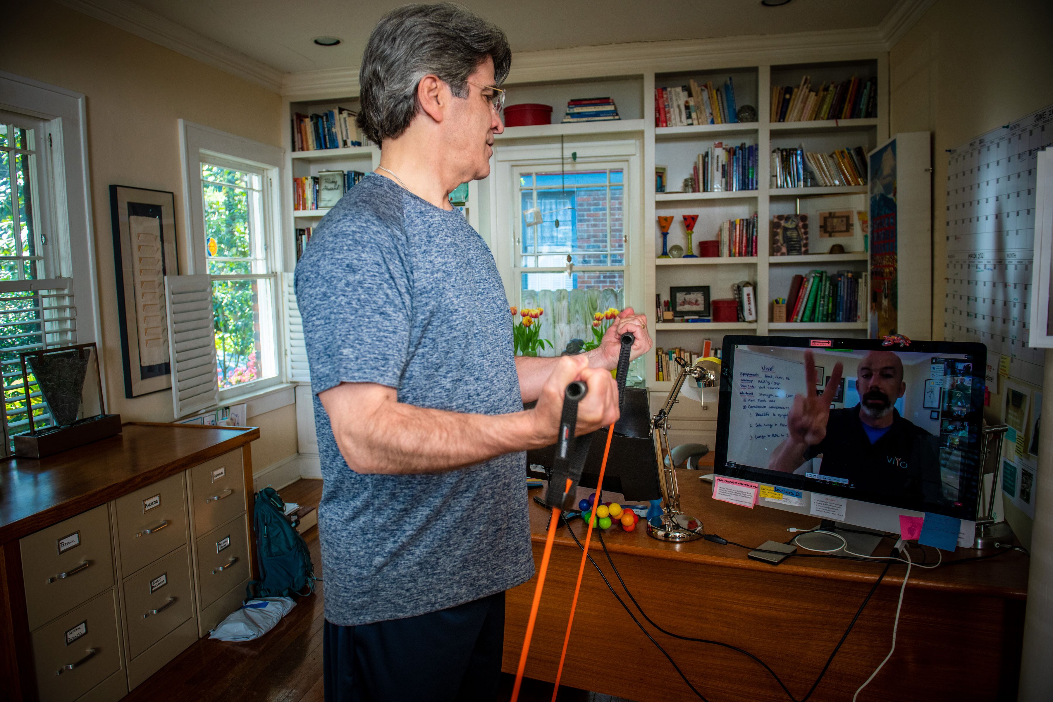 A man uses an exercise band whle looking at a screen.