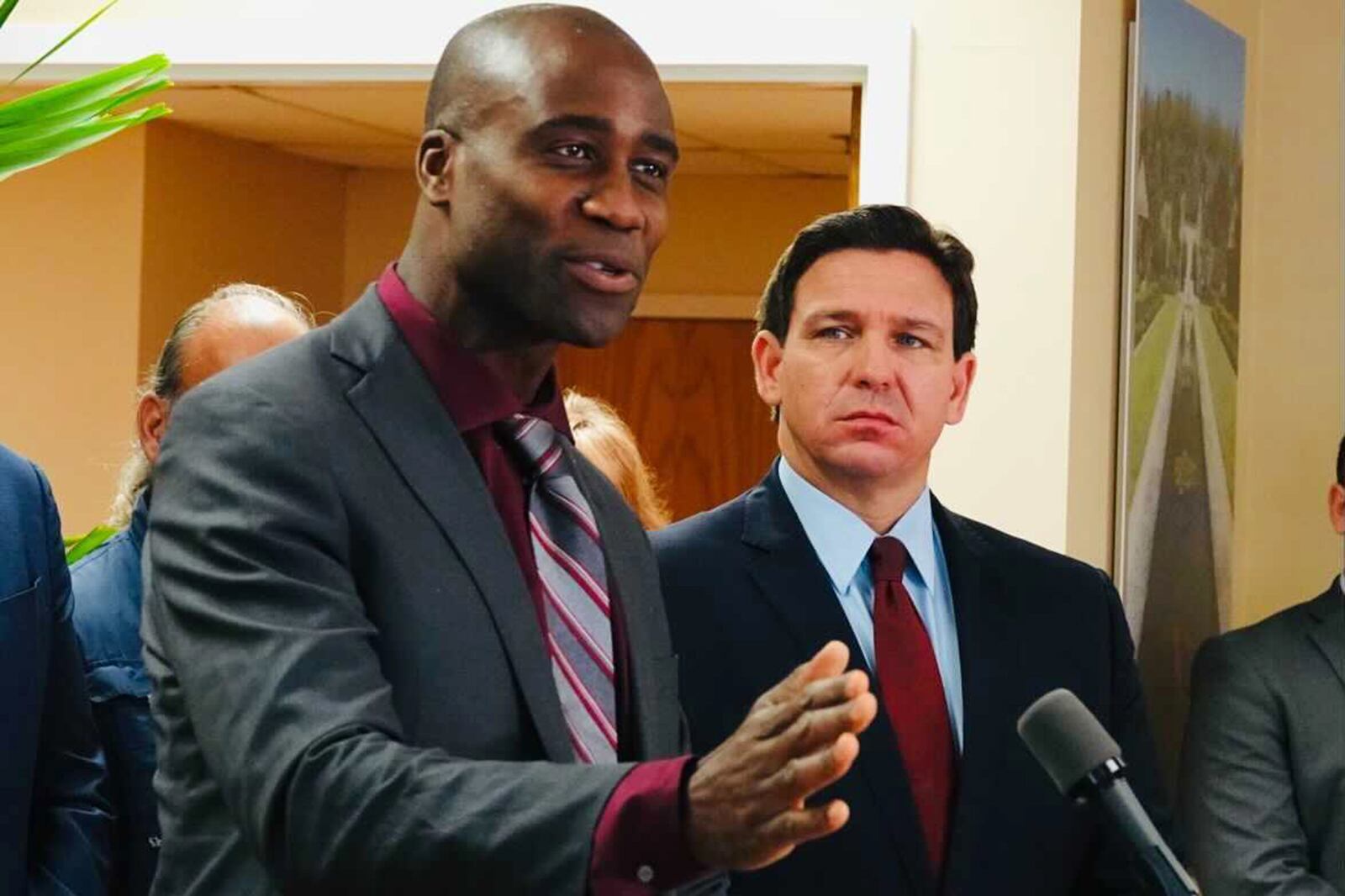 Florida Surgeon General Joseph Ladapo and Gov. Ron DeSantis stand at a podium in front of a microphone.