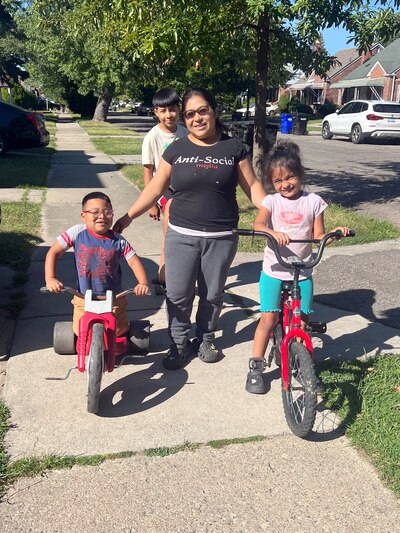 An adult poses for a portrait with three kids on a sidewalk outside in a neighborhood.