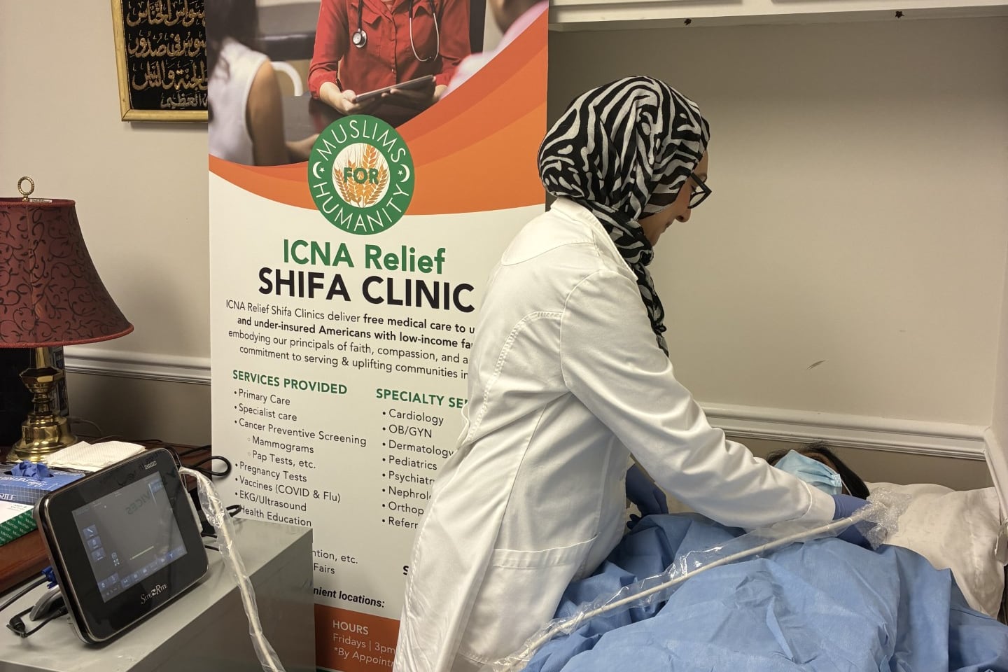 A portrait of a medical worker providing an ultrasound to a patient in front of a sign that says ICNA Relief SHIFA Clinic.
