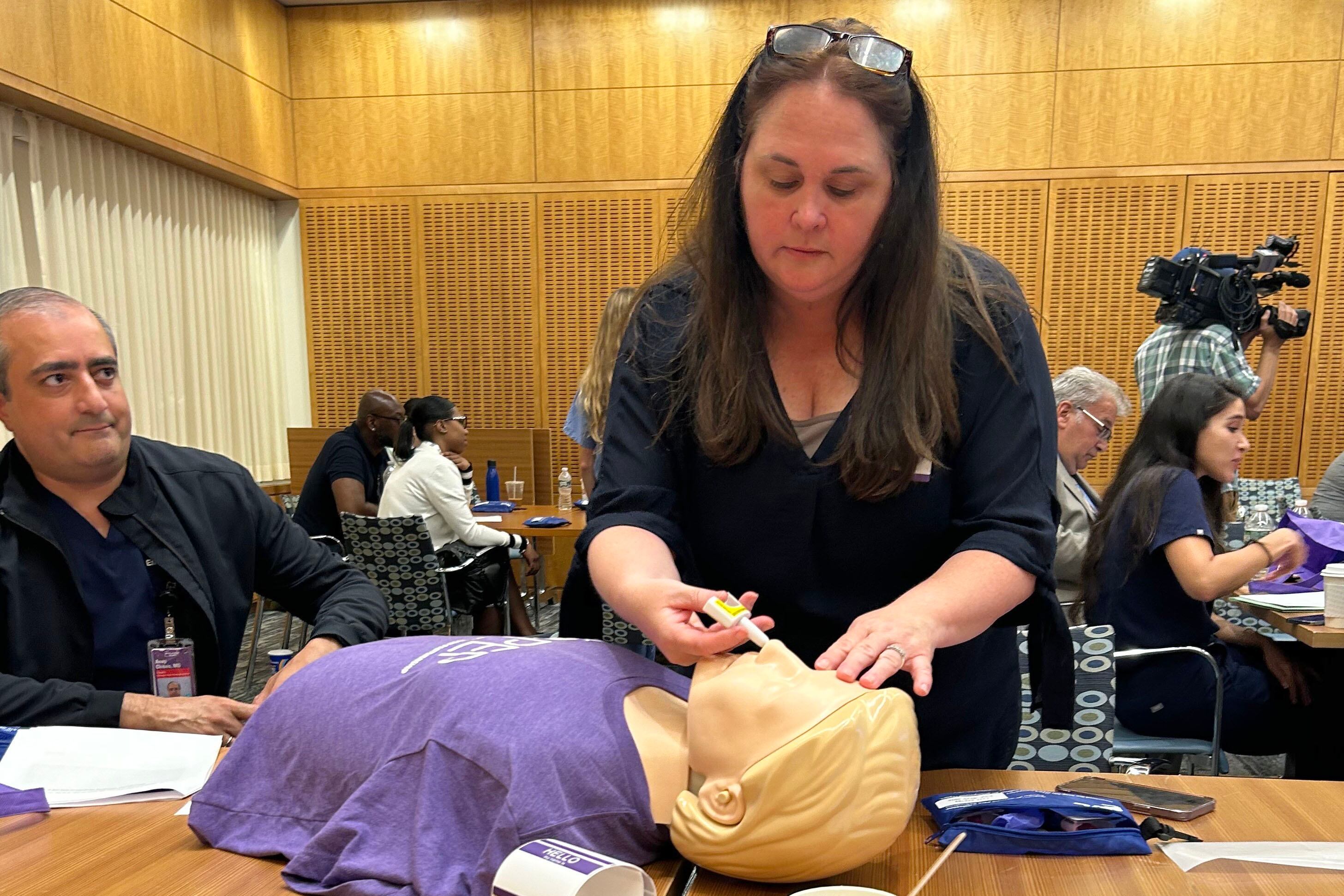 A woman with long dark hair practices giving narcan to a practice doll.