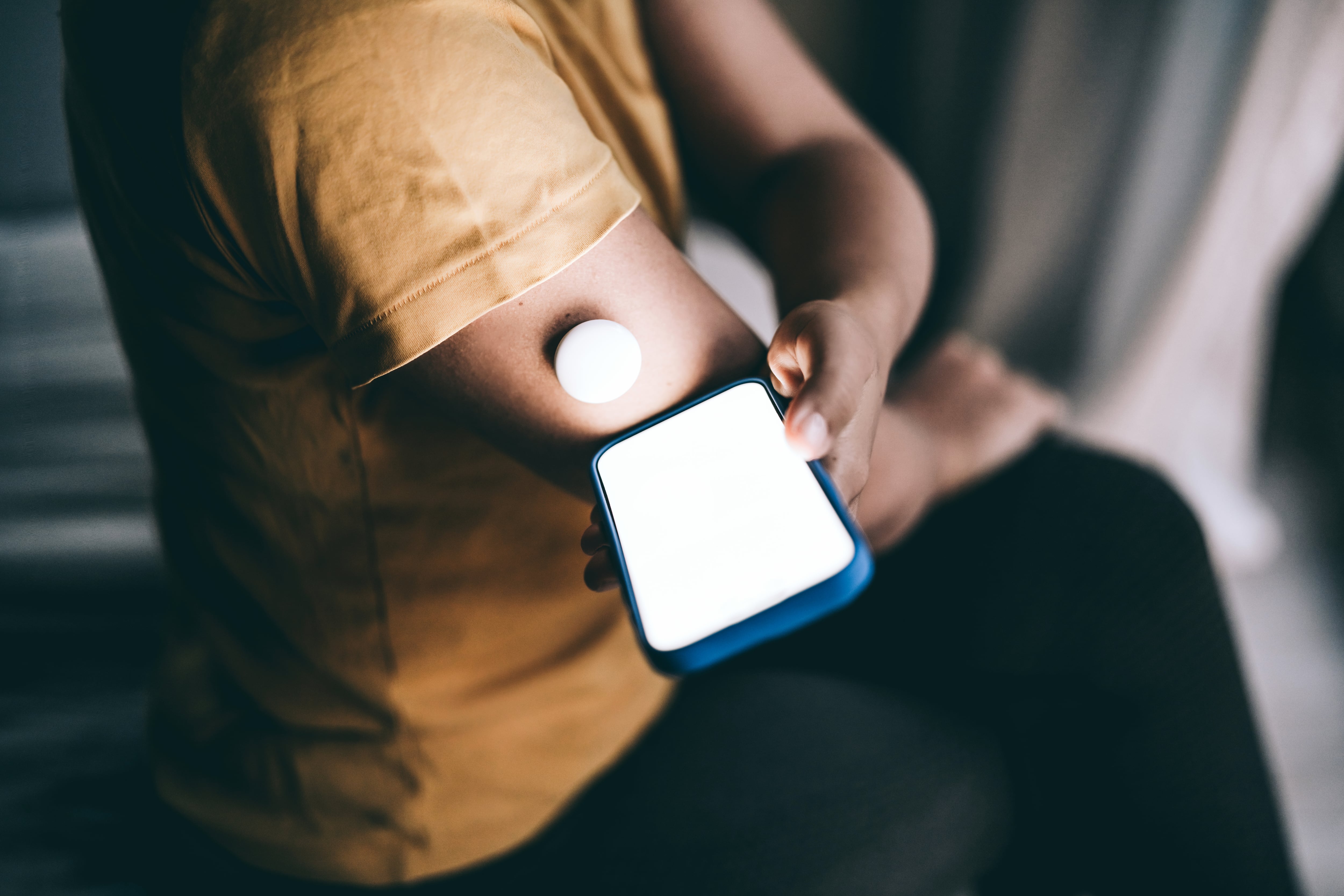 A person uses a glucose monitor on the arm and checks the mobile app for more blood sugar level data.