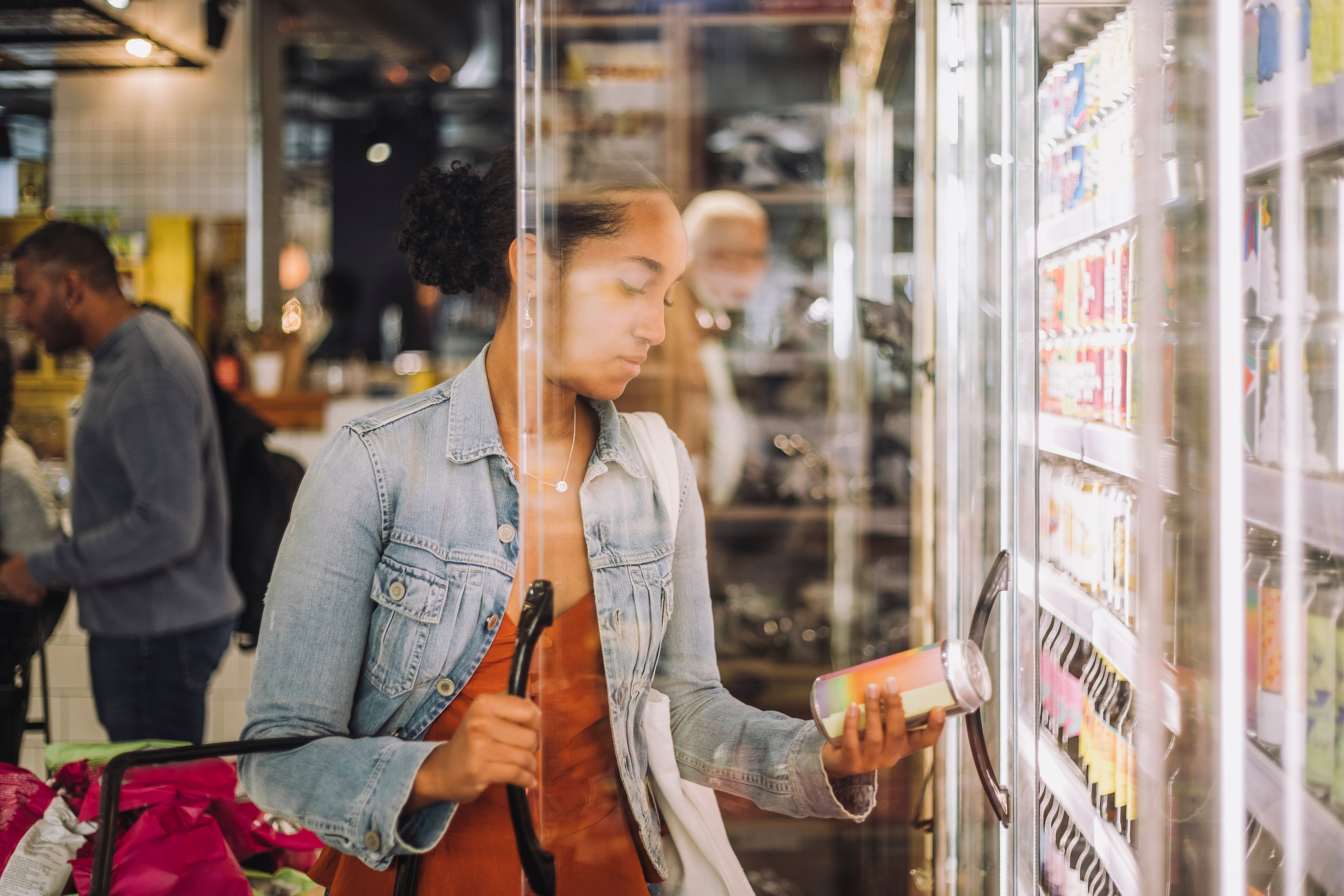A woman examines a product label from a refrigerator in a grocery store.