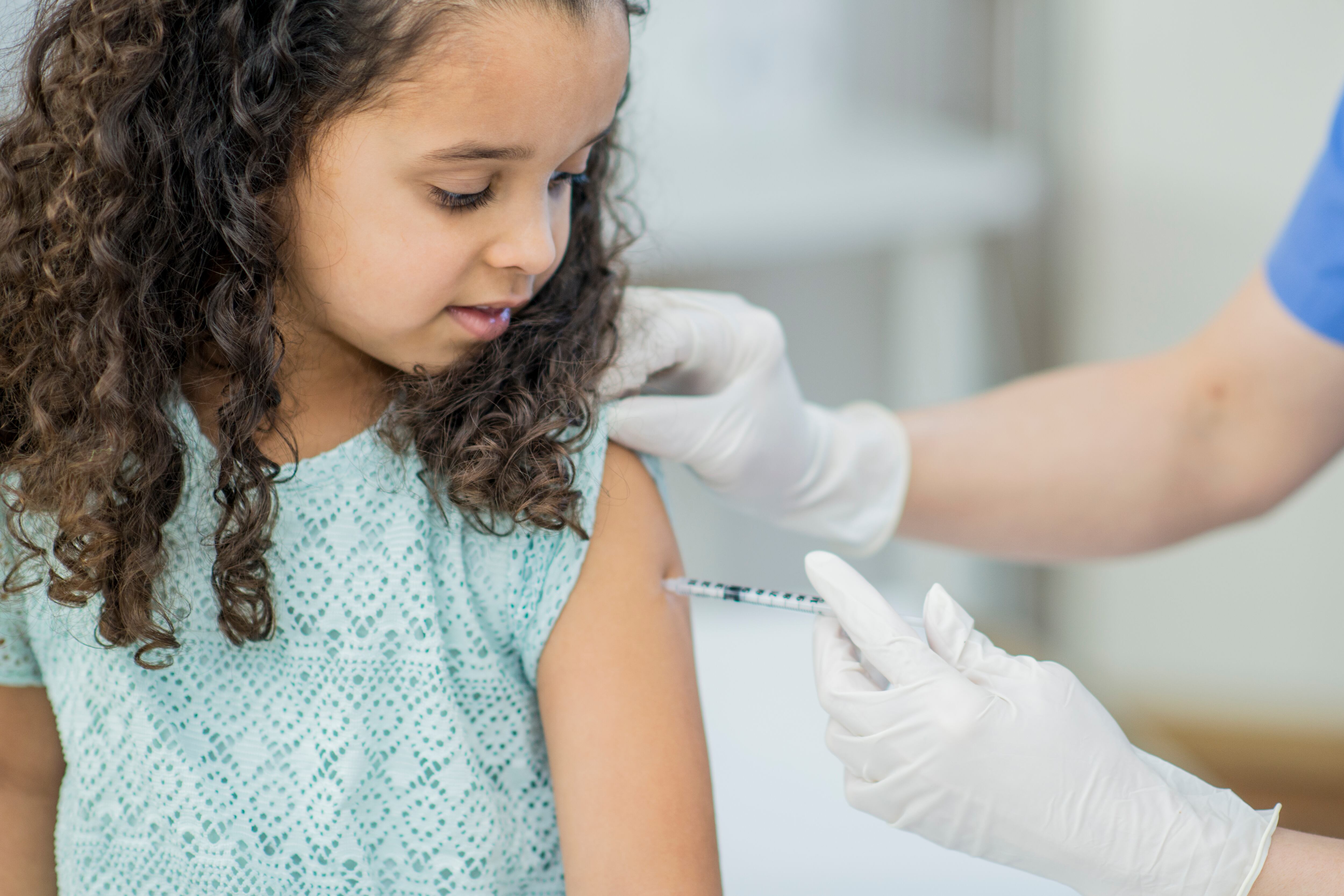 A young girl gets a shot in the arm in a doctor's office.