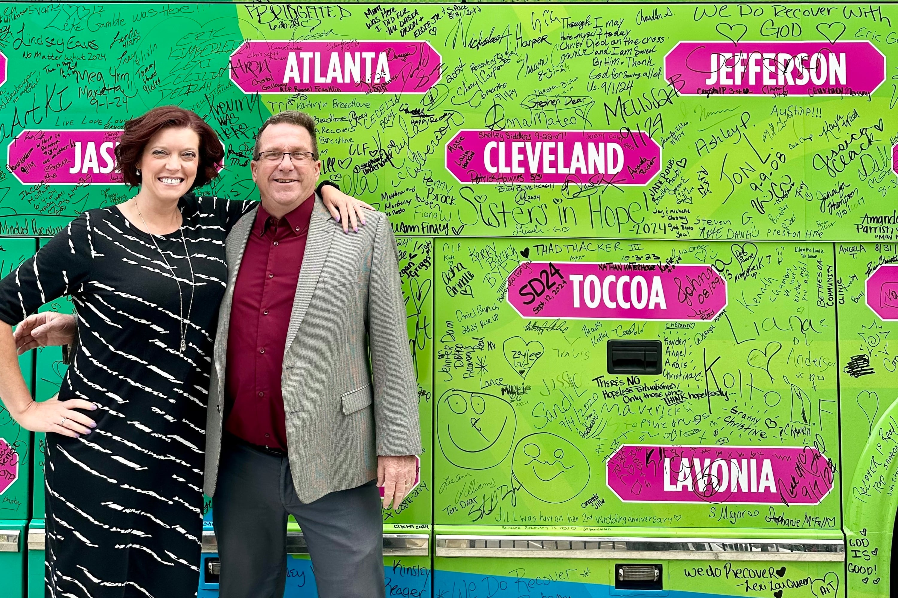 Courtney Robinson and Greg Gardner stand in front of a colorful bus.