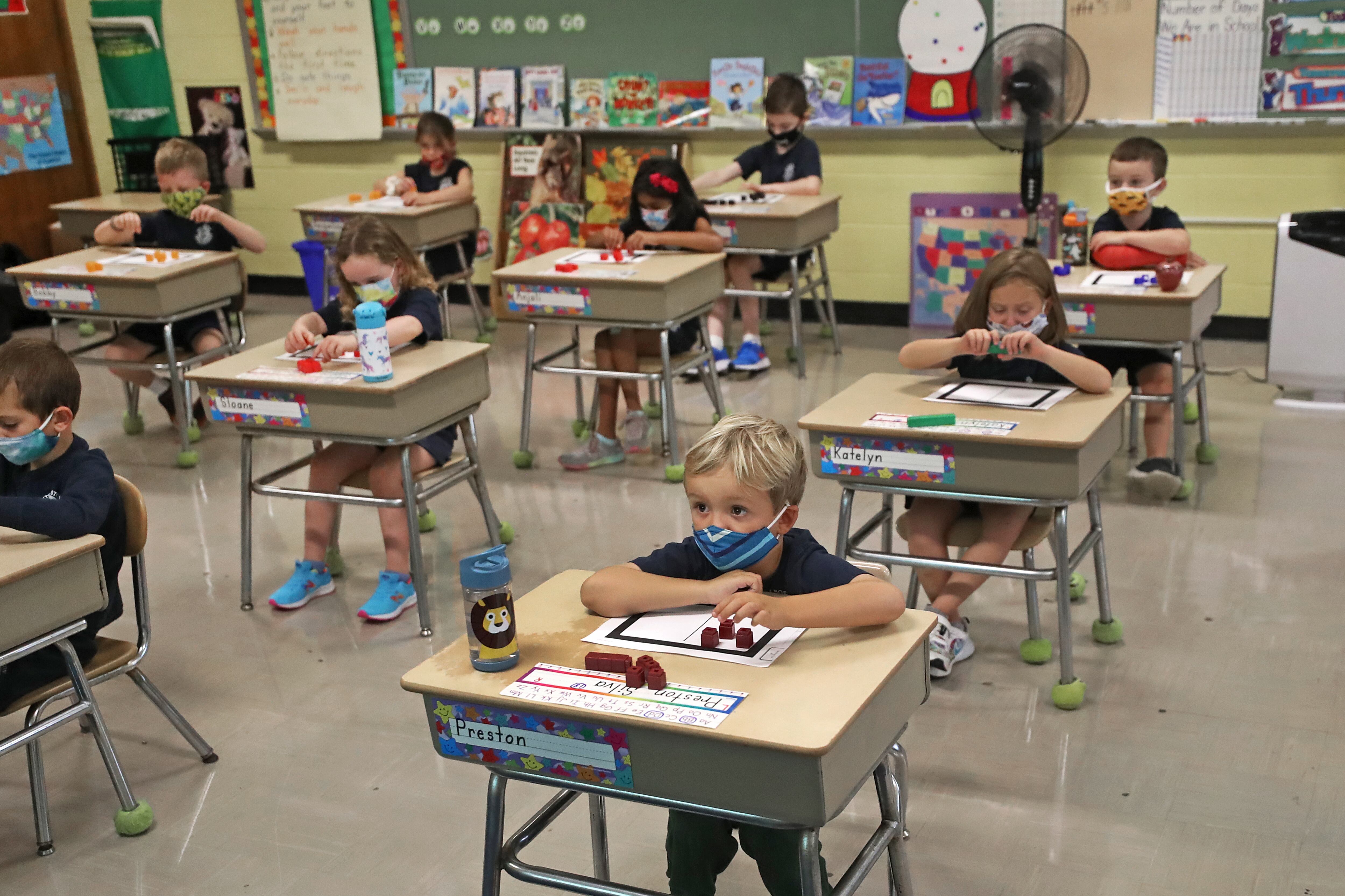Children wearing face masks are seated at desks in a classroom.