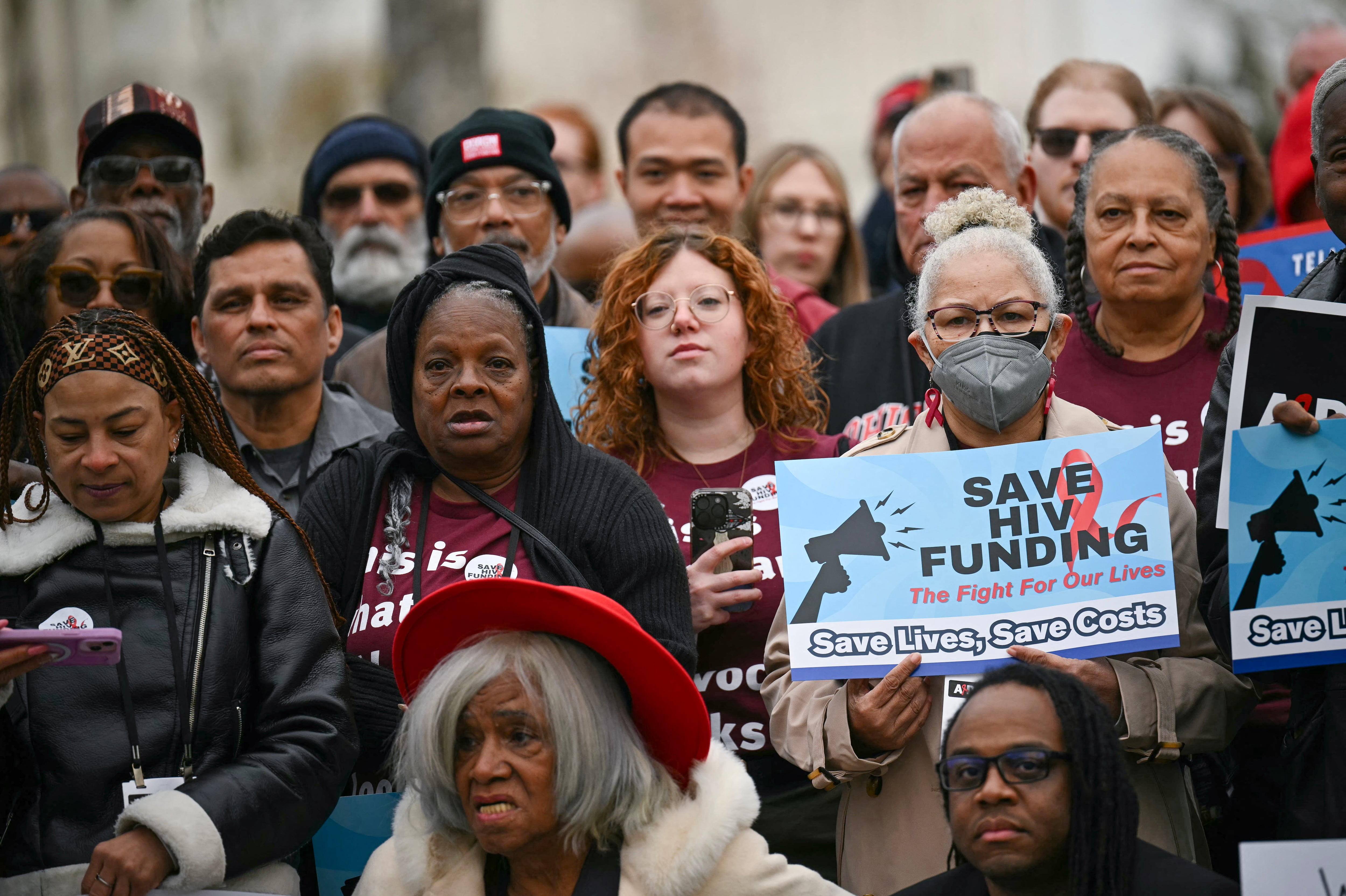 People gather with signs to protest federal HIV funding cuts.