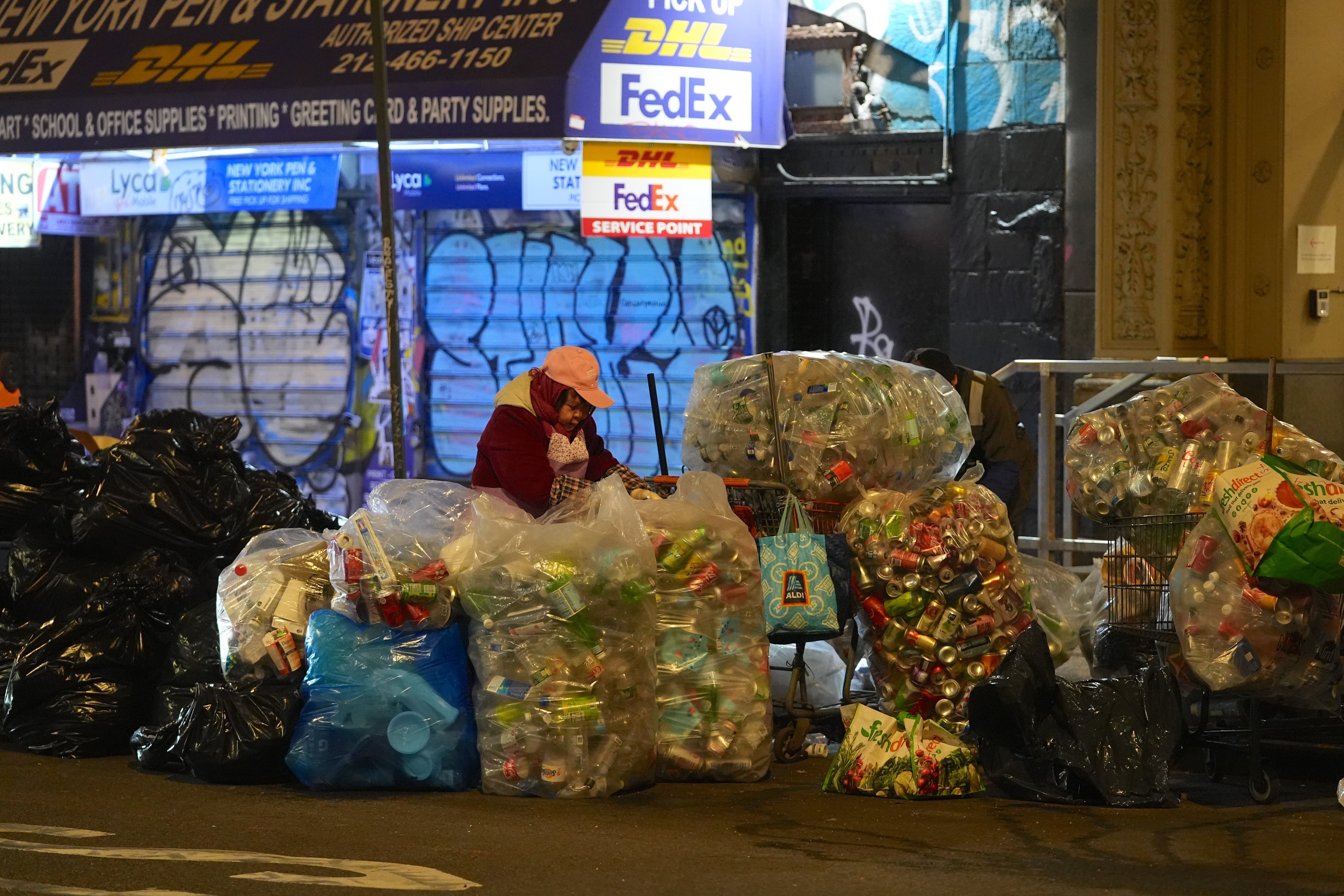 A person stands amid piles of filled garbage bags on a New York City sidewalk.