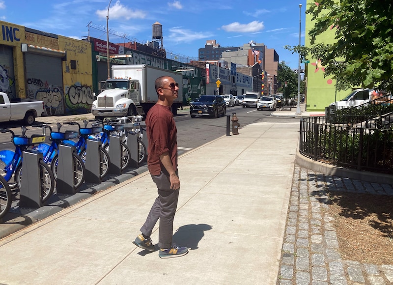 A person wearing a dark red shirt walks down a sidewalk next to a row of bikes and a white semi-truck in the background.
