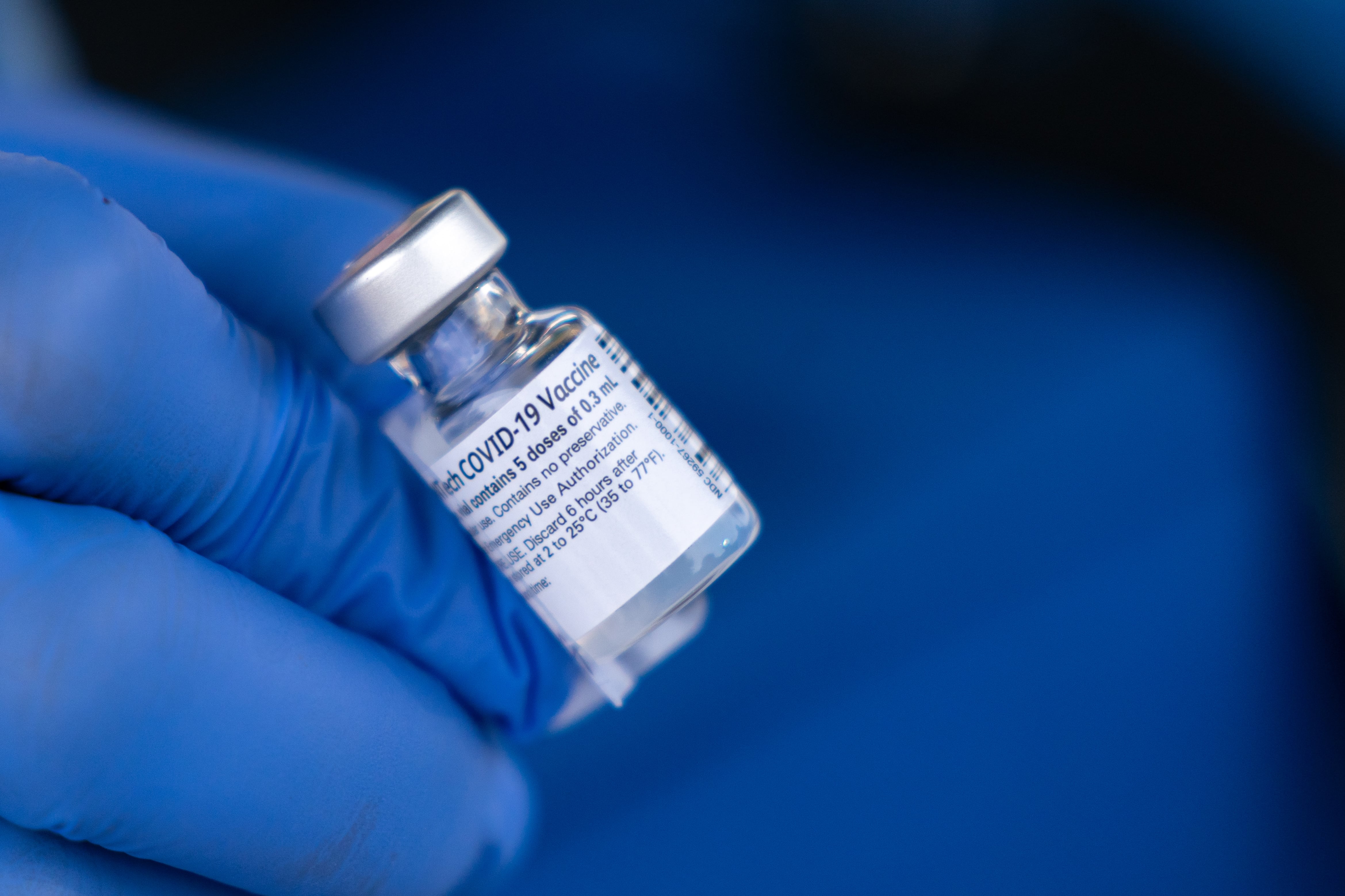 A hand wearing a blue medical glove holds a vial of Covid-19 vaccine.