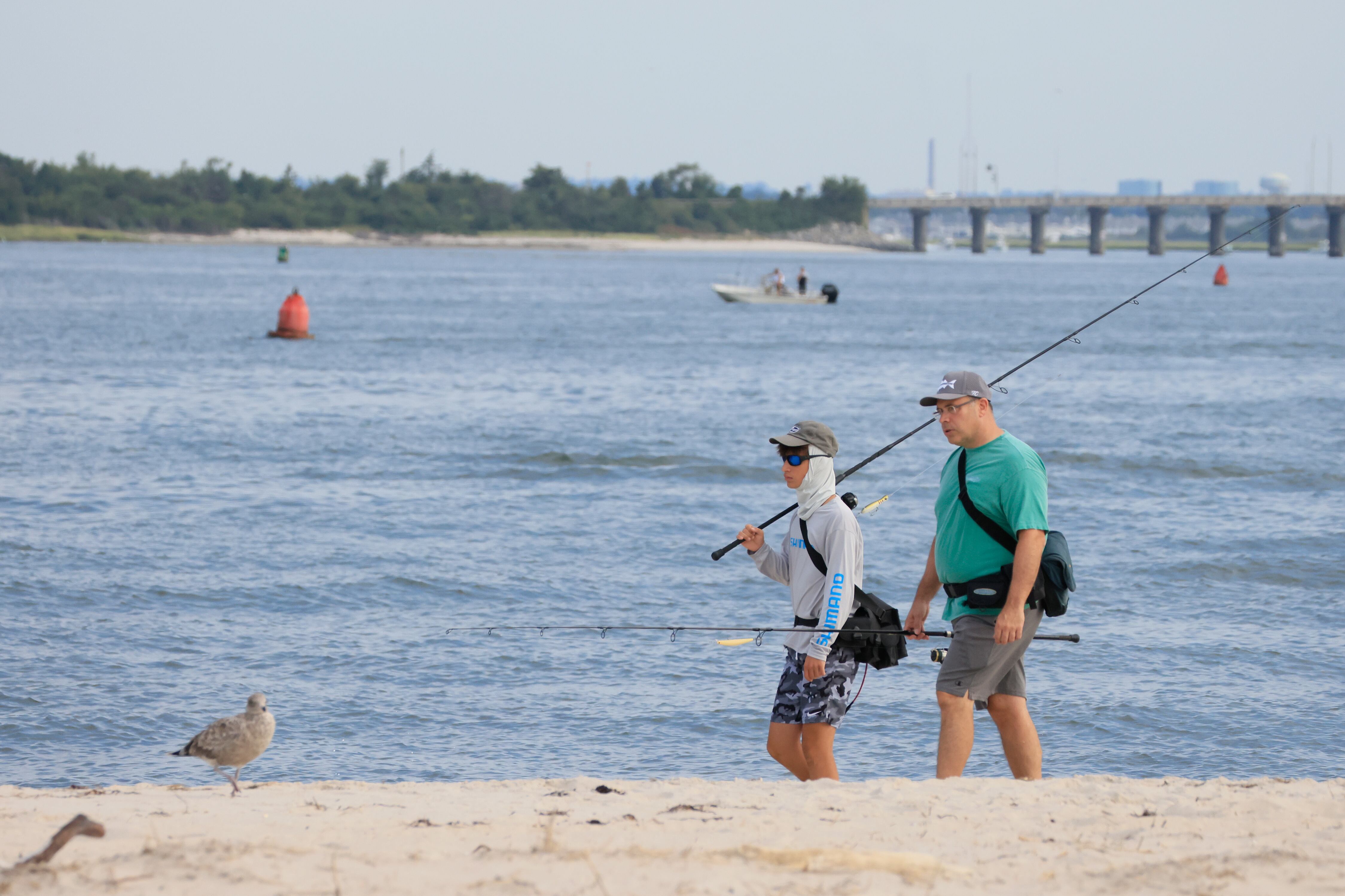 Two men walk along the beach carrying fishing poles.