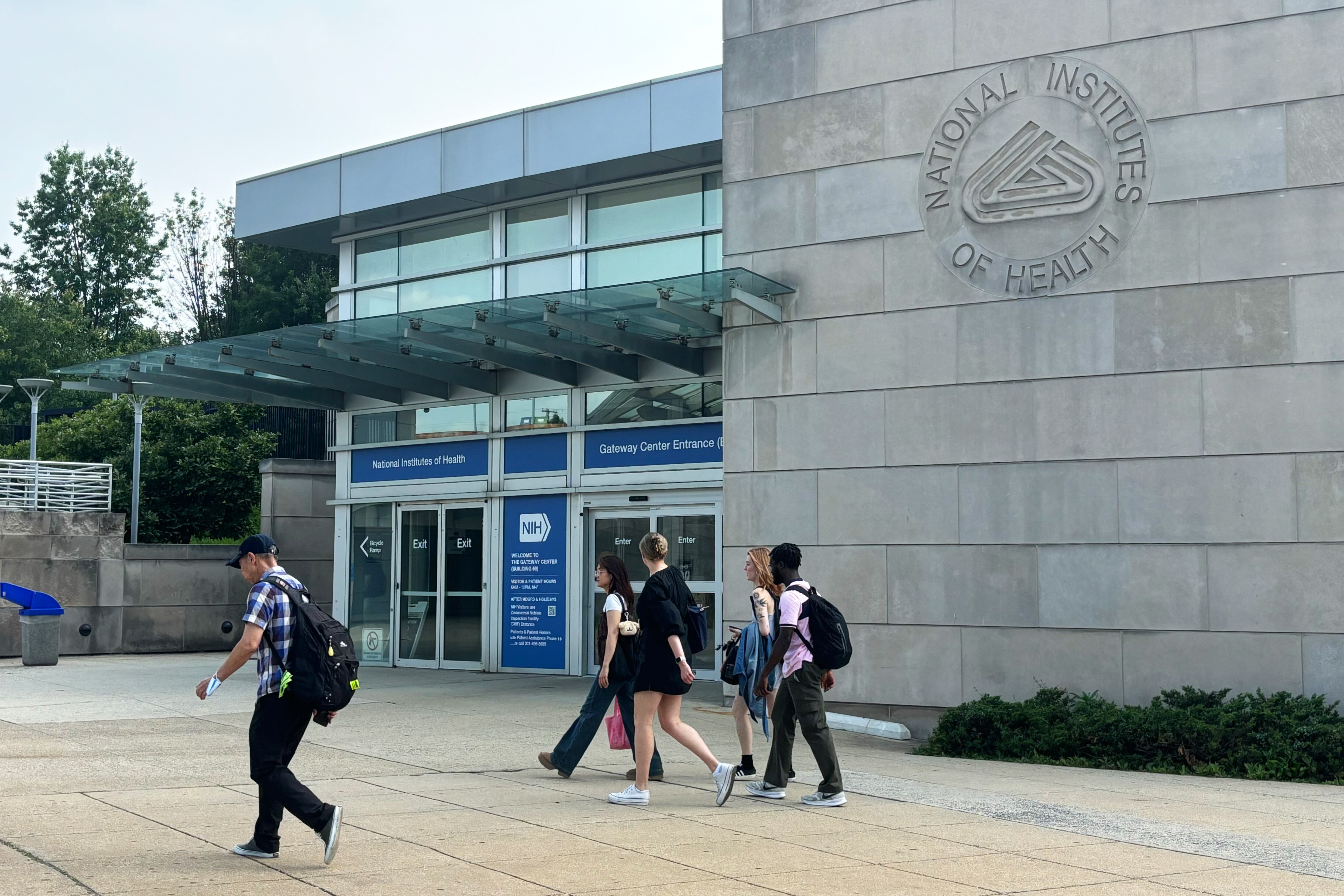 People walk past an entrance to the National Institutes of Health campus.