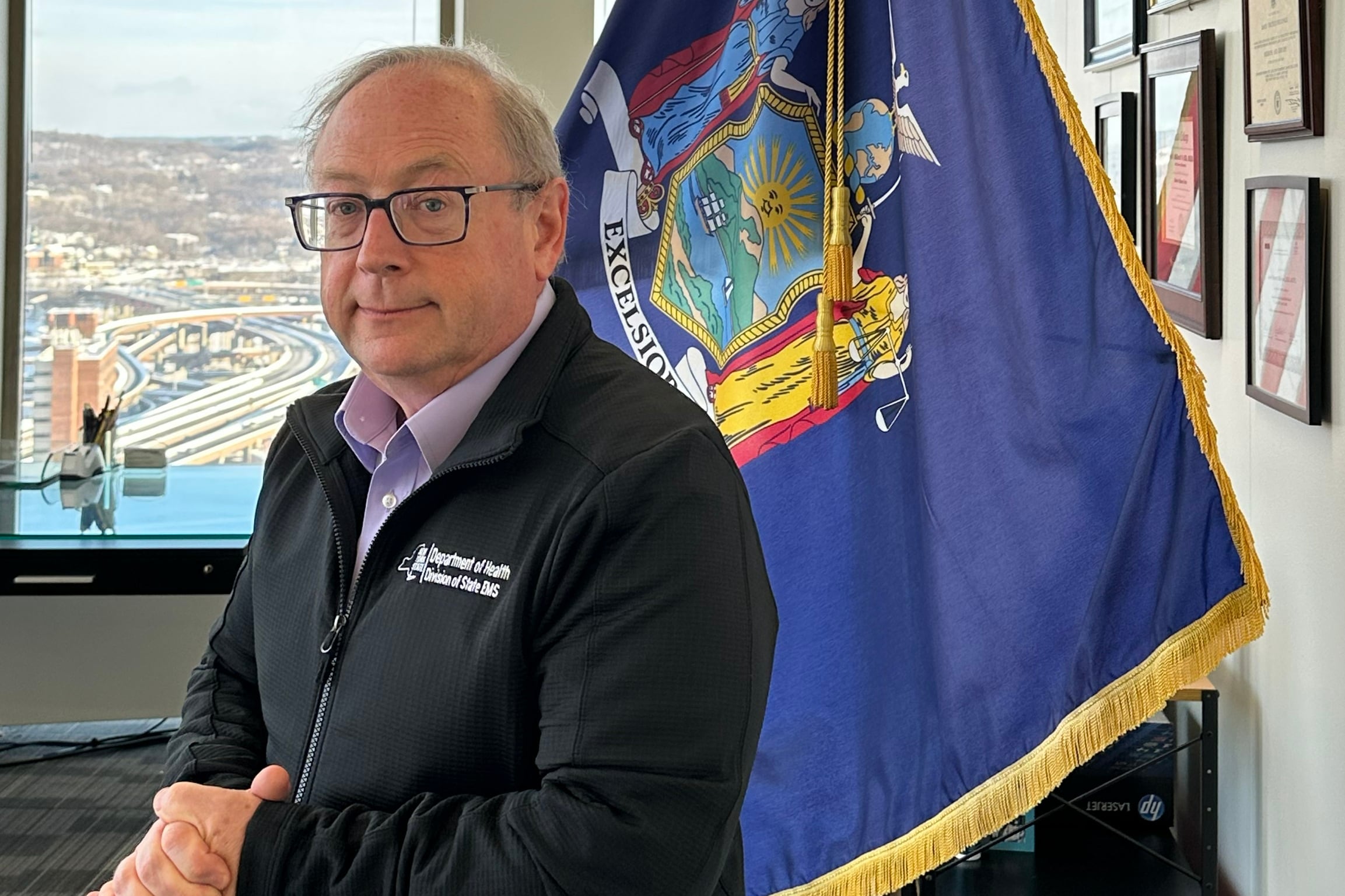 New York State Health Commissioner Dr. James McDonald stands in front of a flag in his office.