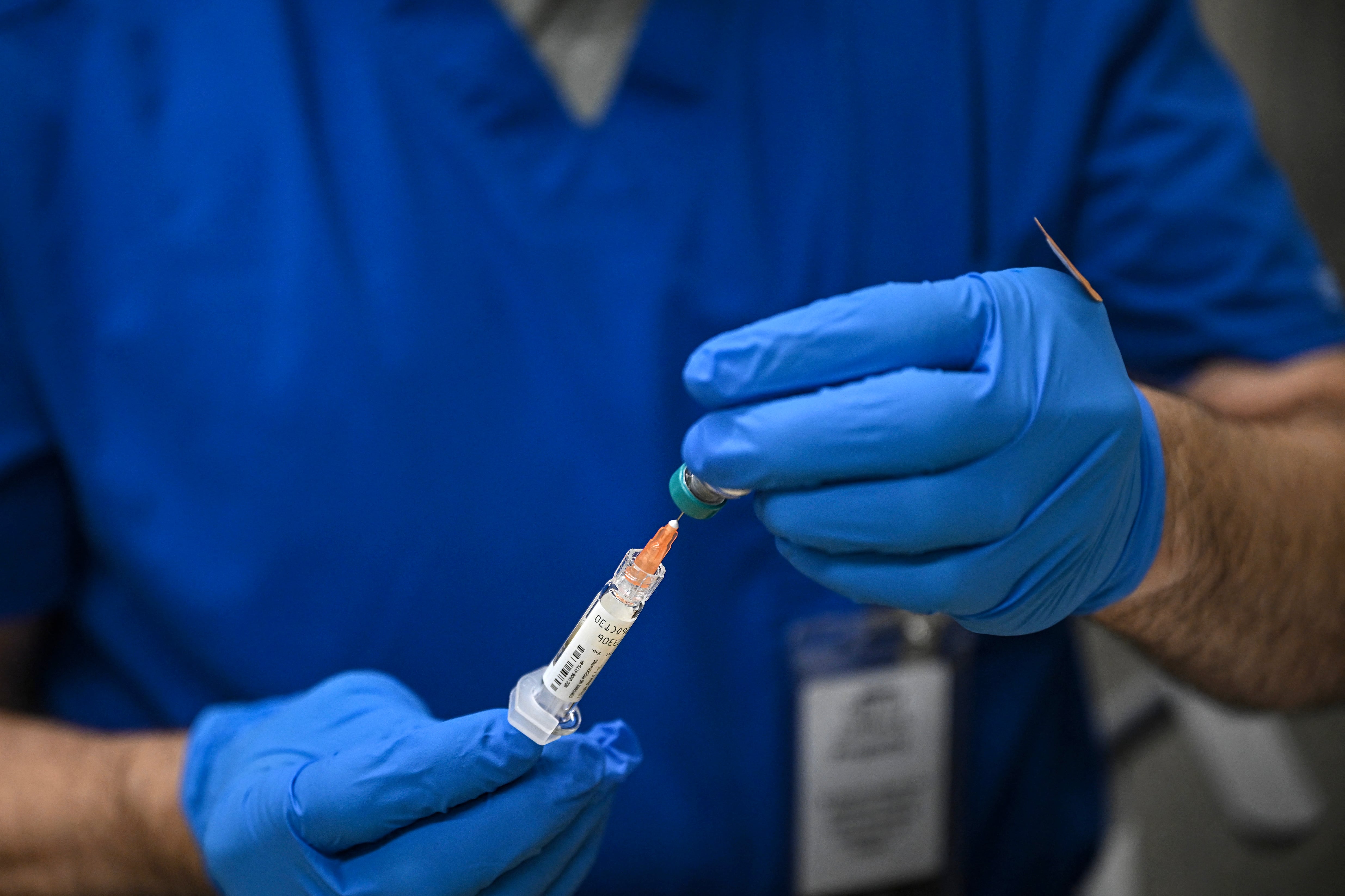 A close up of a pair of hands in blue gloves holding a syringe and a bottle of measles vaccine.