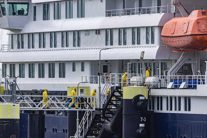 A photograph of six health workers in yellow hazmat suits on a large cruise ship.