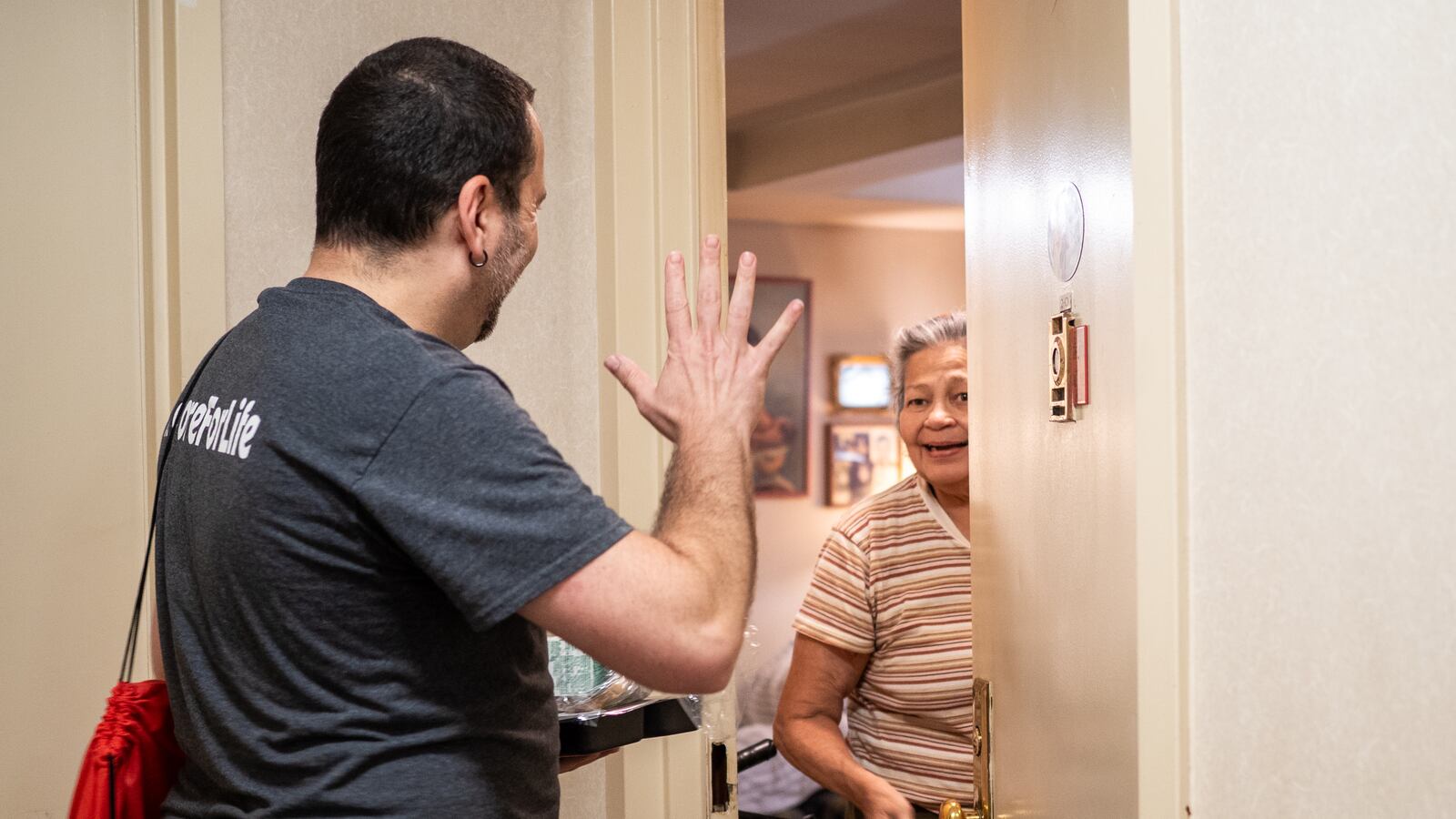 A man in a gray t-shirt raises his hand toward a woman opening a door.