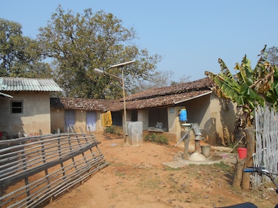 A one-story small building features a blue handwashing station, a well, and a solar paneled light.